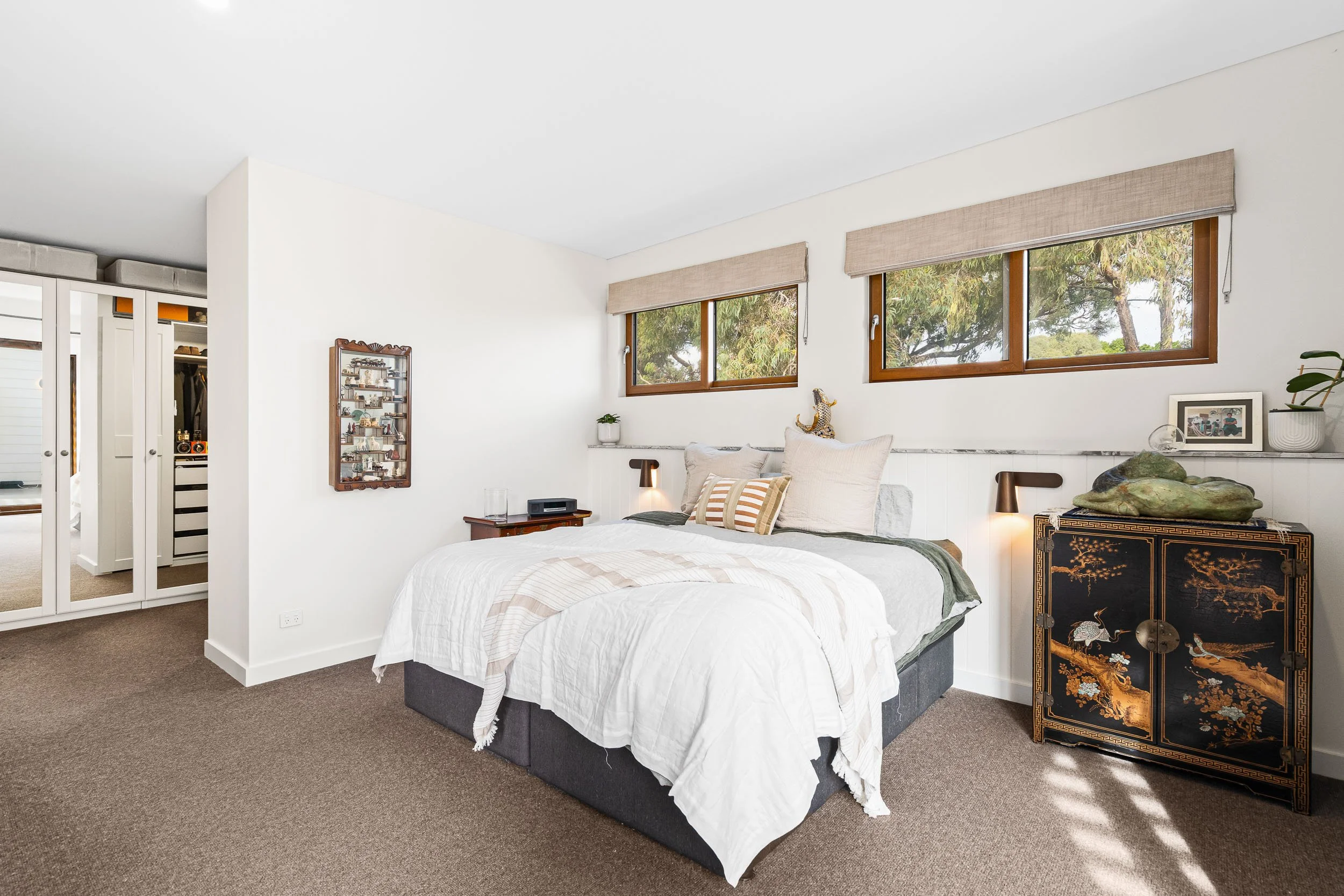 Bedroom with white bedding, timber bedside tables and a wide horizontal window.
