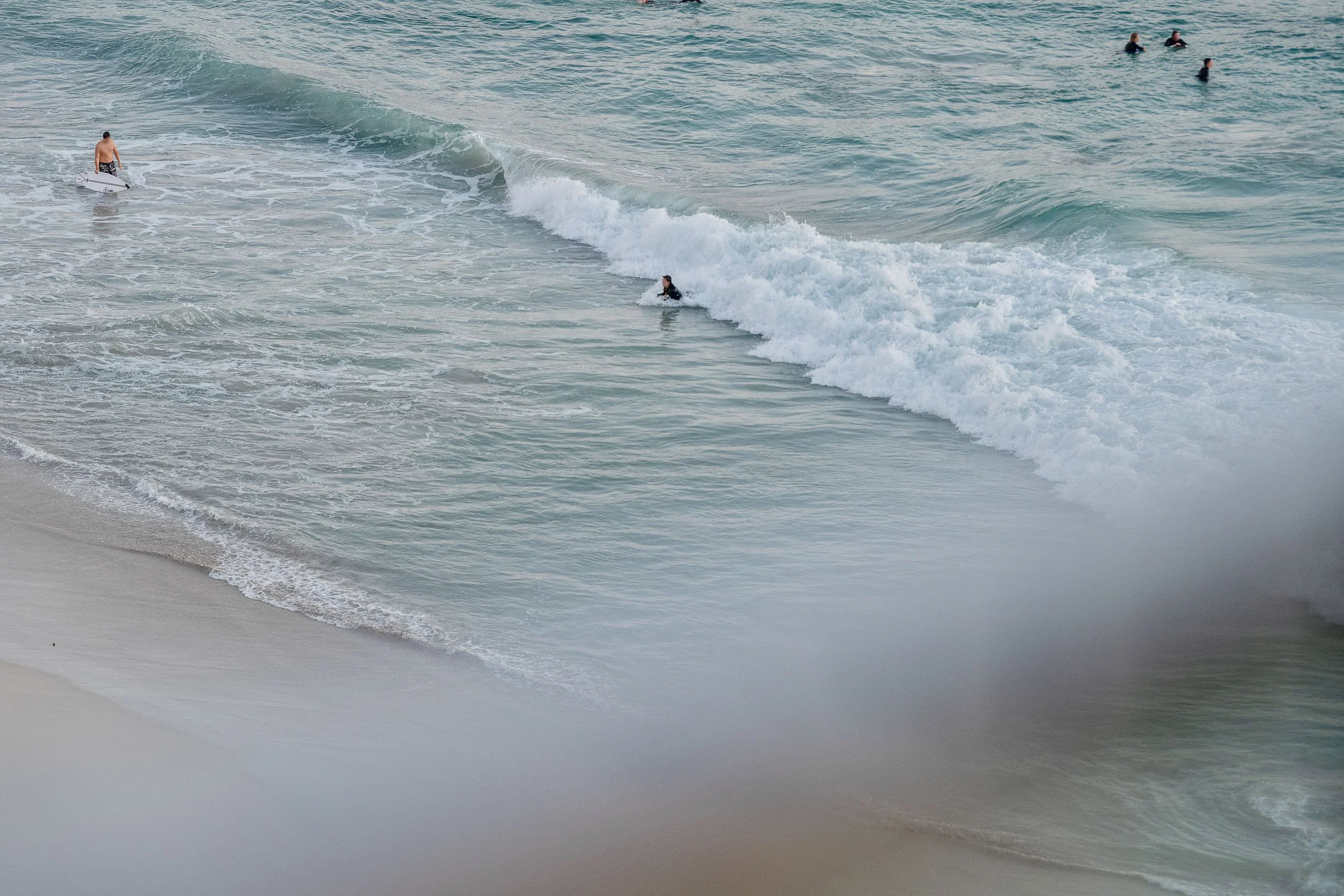 Aerial detail of turquoise waves washing onto a sandy beach.