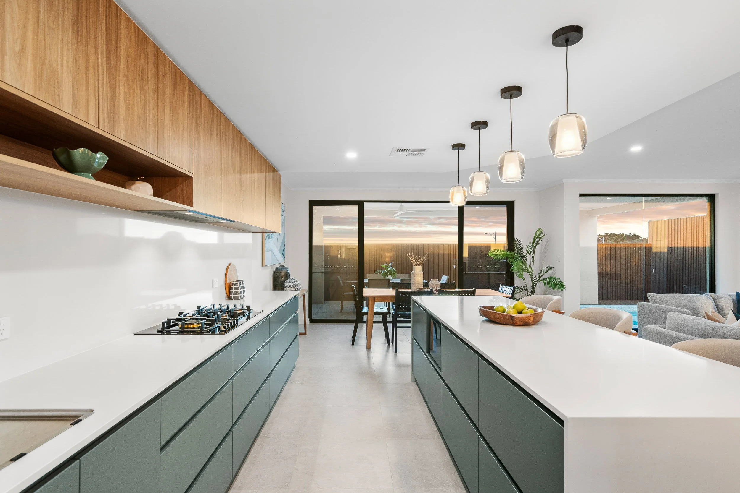 Galley kitchen with muted green cabinetry, white benchtops and pendant lights.