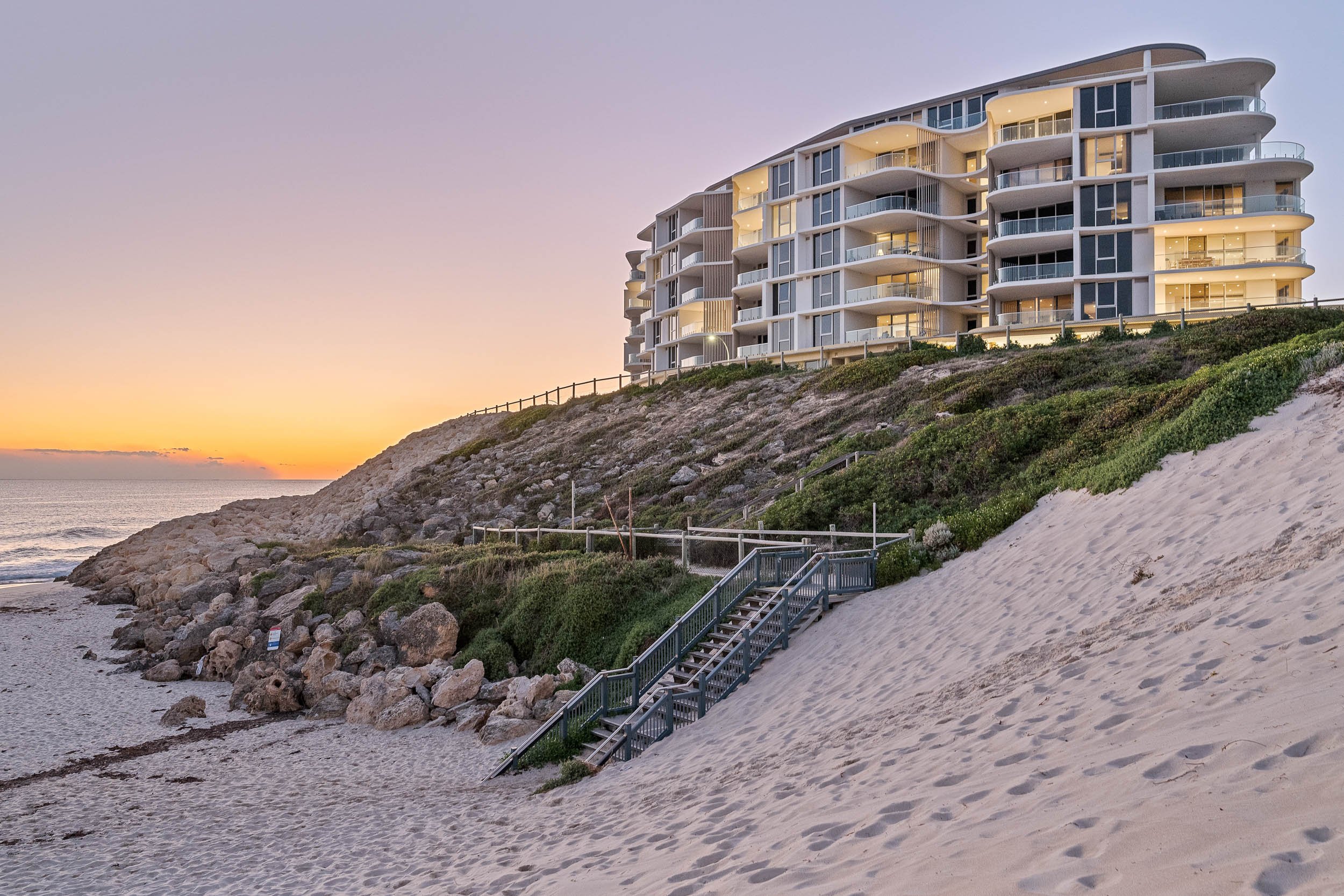 Beachfront apartment building above coastal dunes in the warm light of sunset.