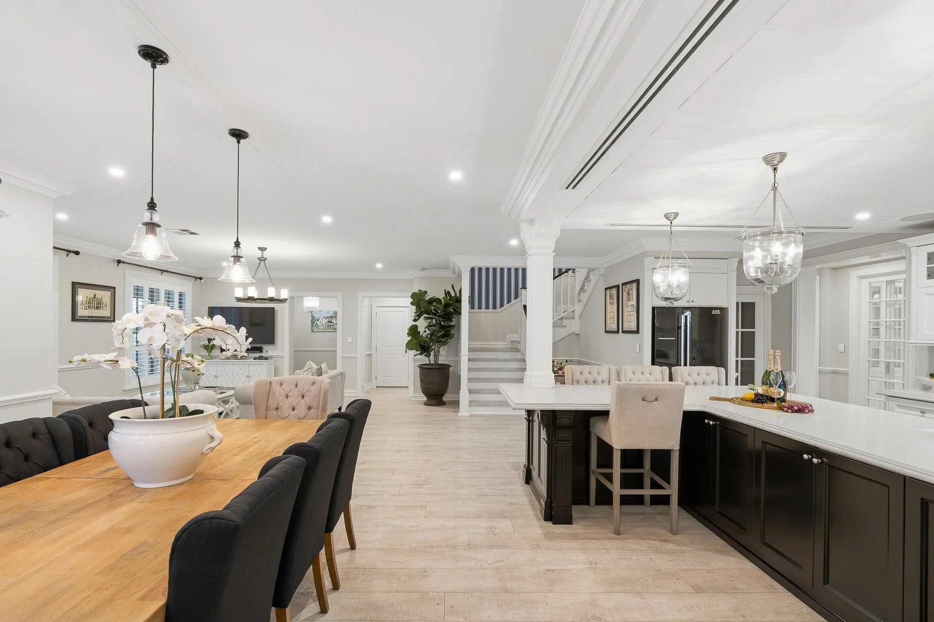 Open-plan dining and kitchen area with a timber table, dark chairs and white cabinetry.