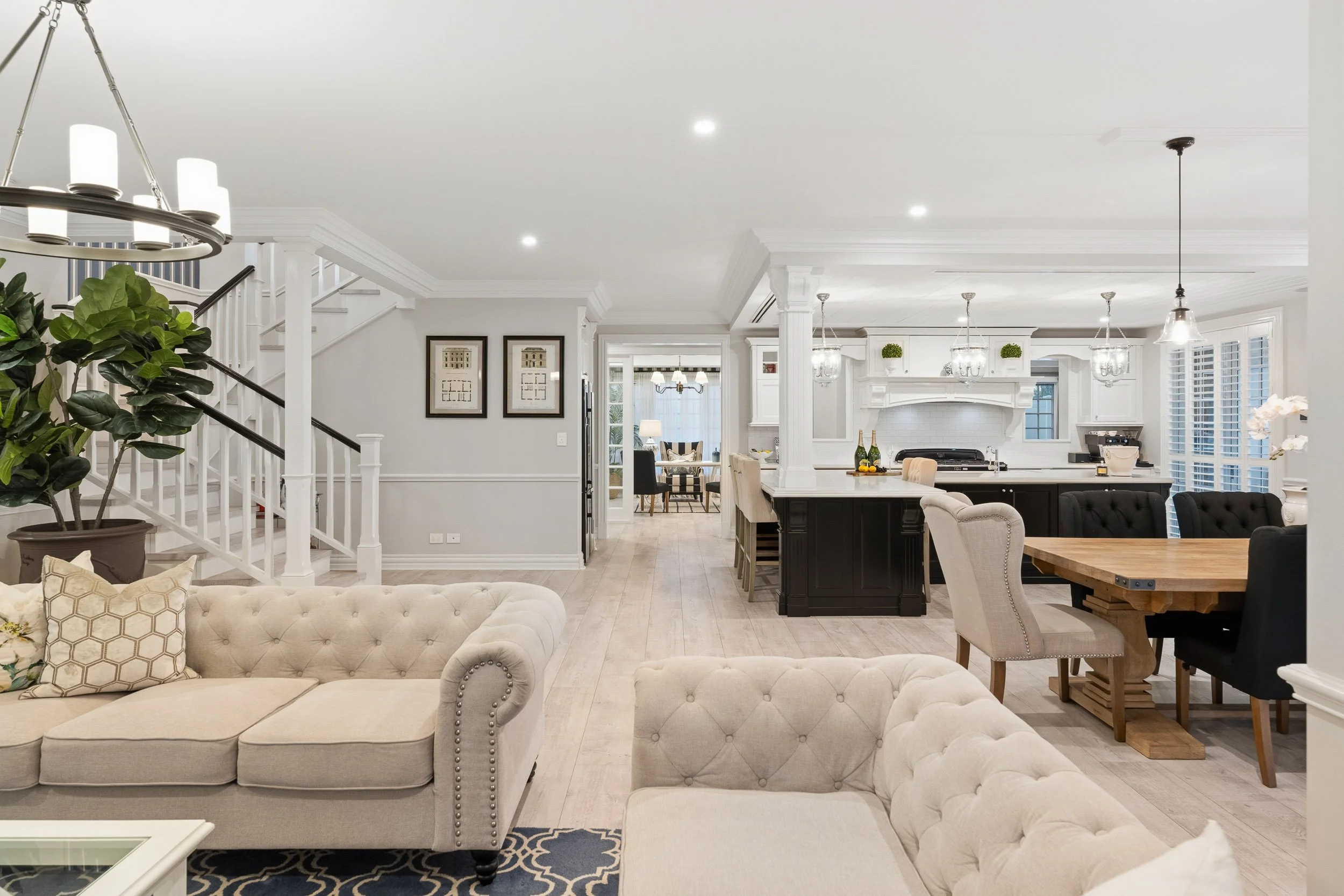 Open-plan living and dining room with tufted sofas, white cabinetry and a dark kitchen island.