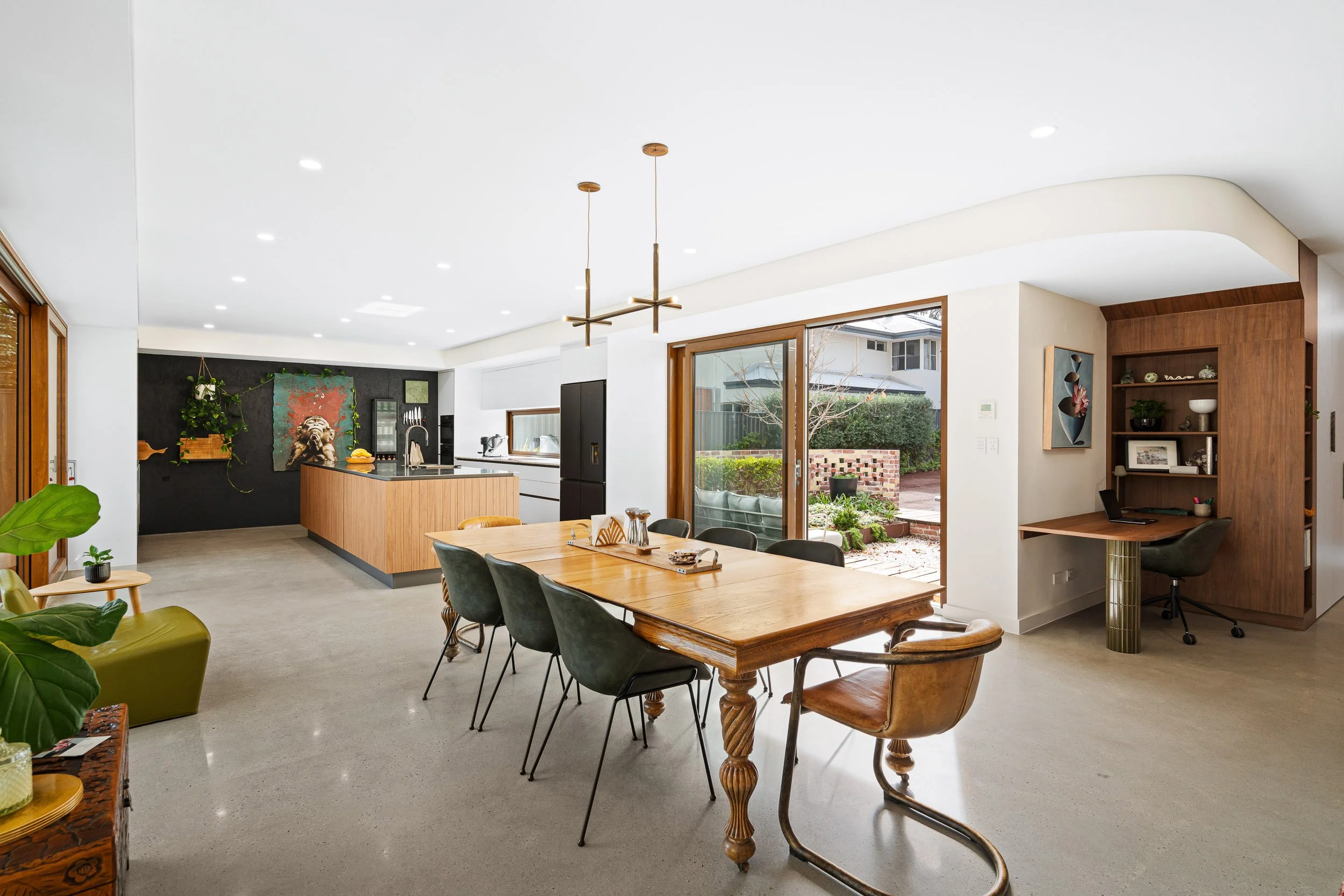 Dining room with a timber table, upholstered chairs, pendant lighting and colourful artwork.