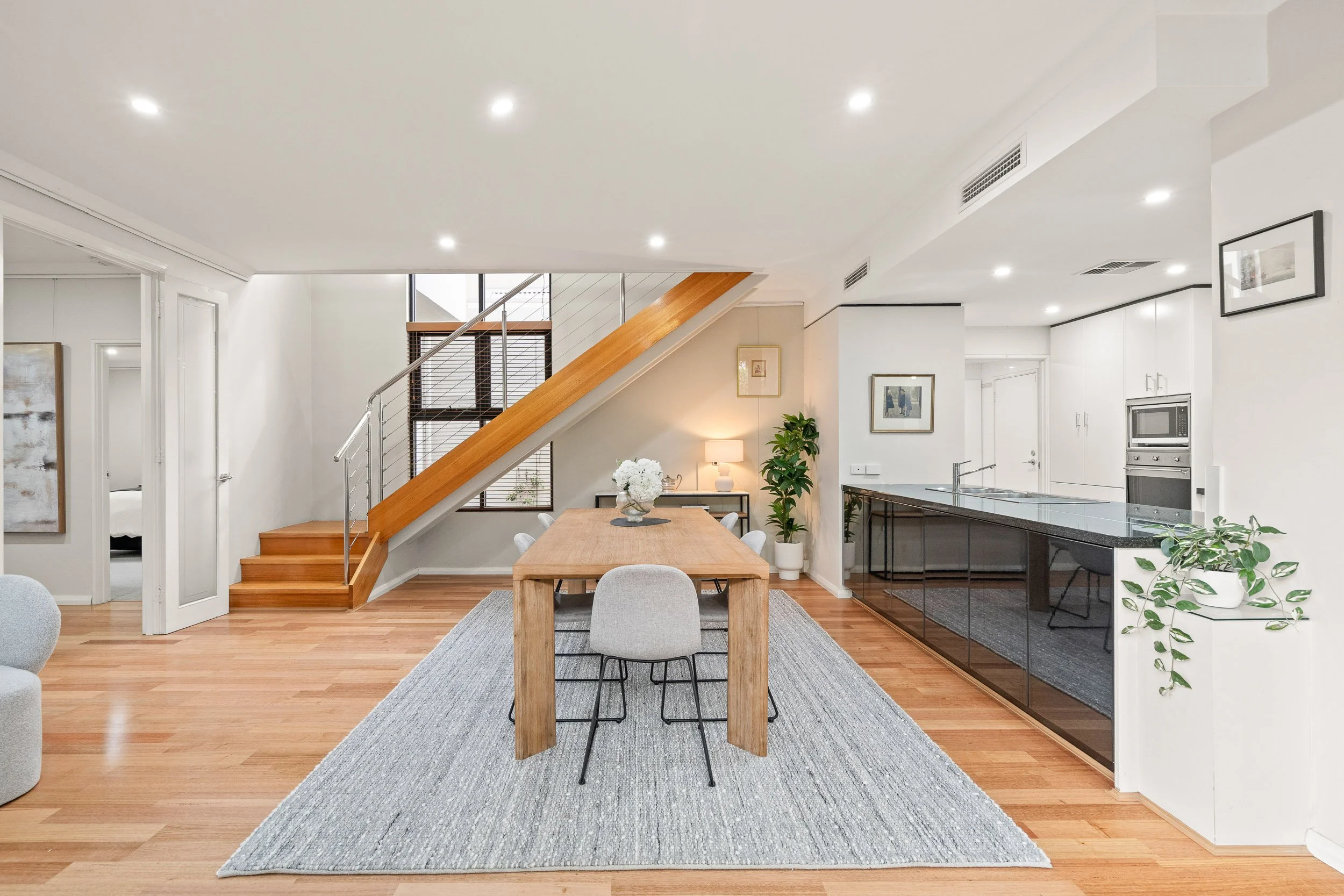 Open-plan dining area with a round table, woven chairs and a timber staircase.
