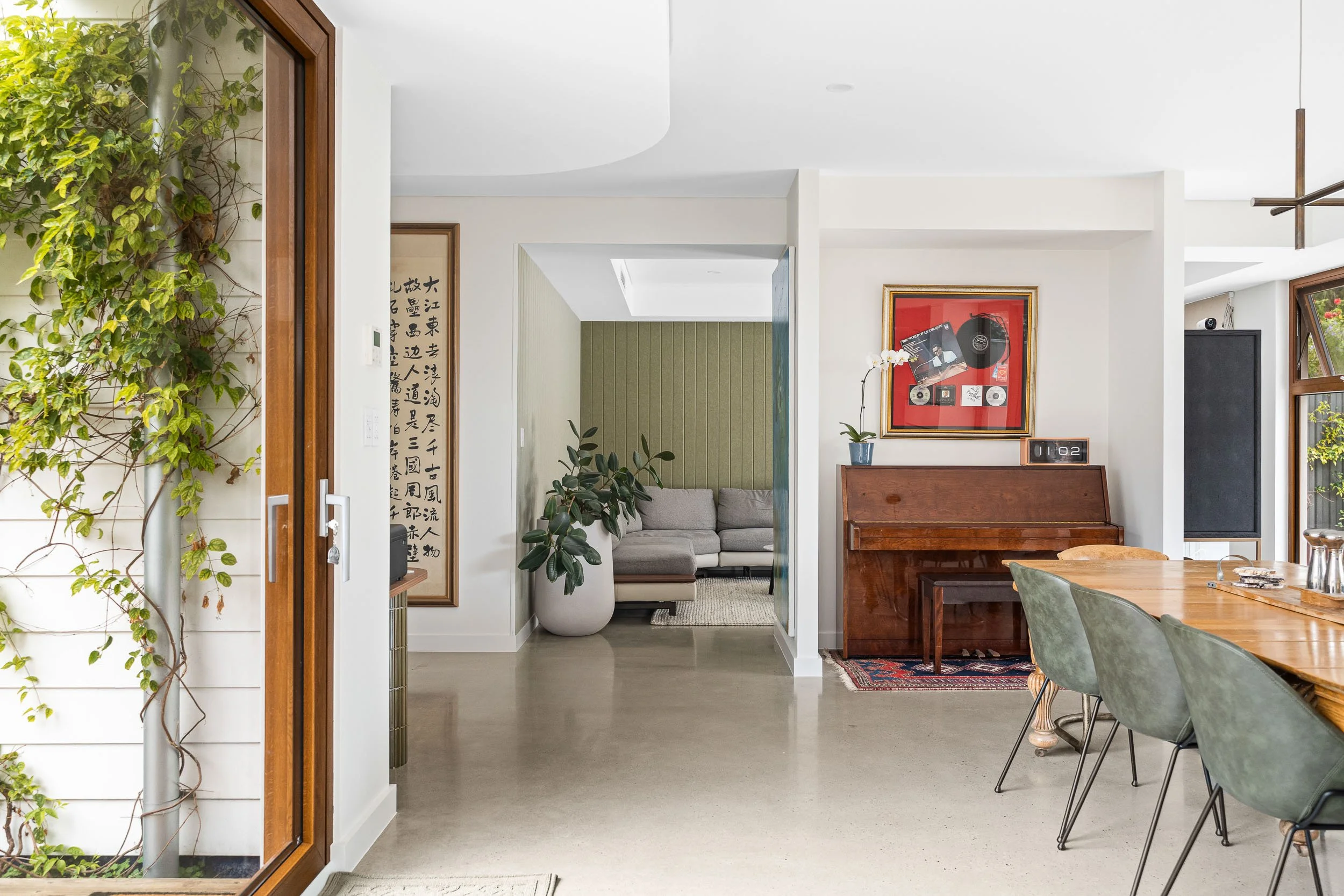 Living area with an upright piano, framed artwork and an adjoining bright room.