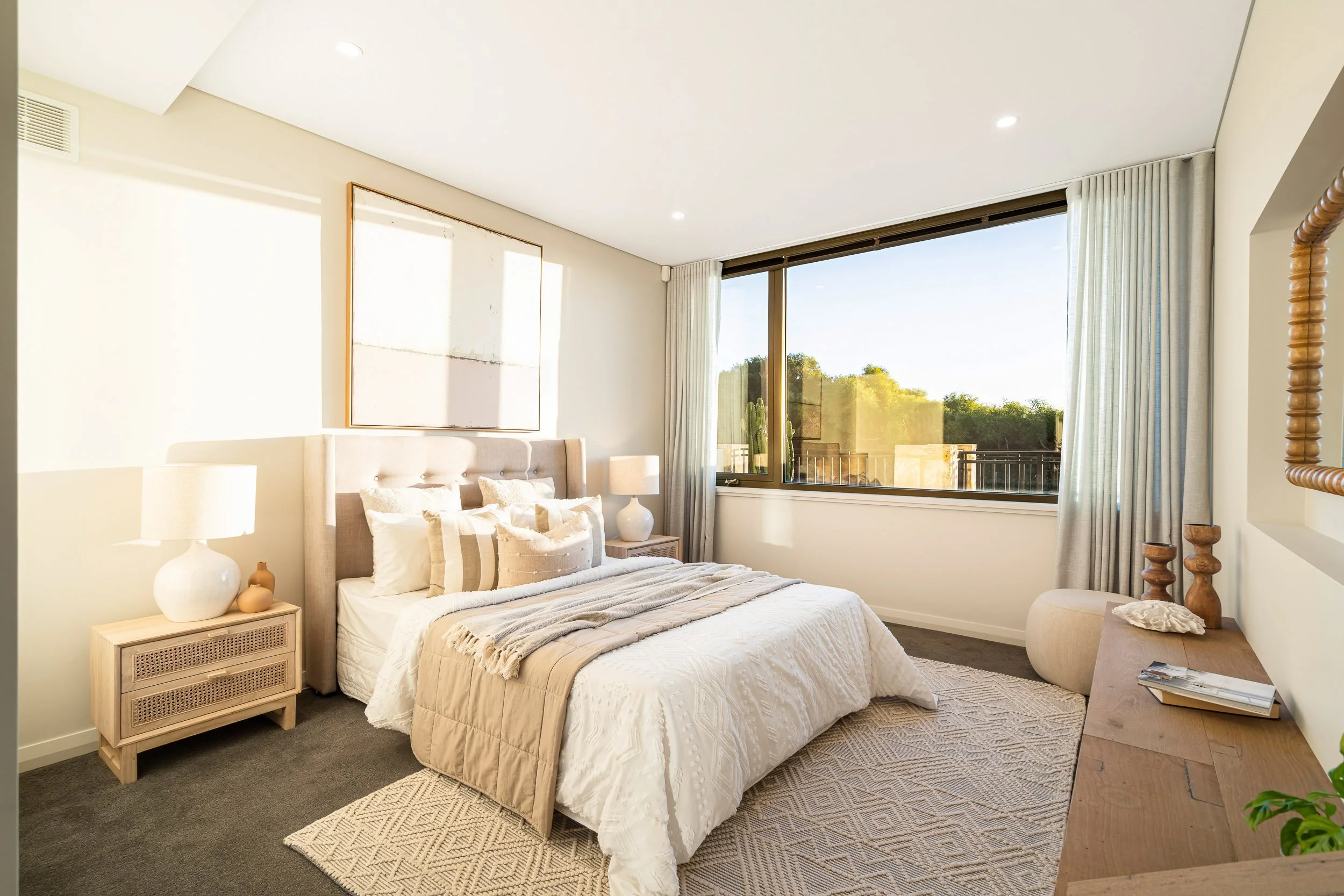 Bedroom with pale furnishings and corner windows overlooking the coast.