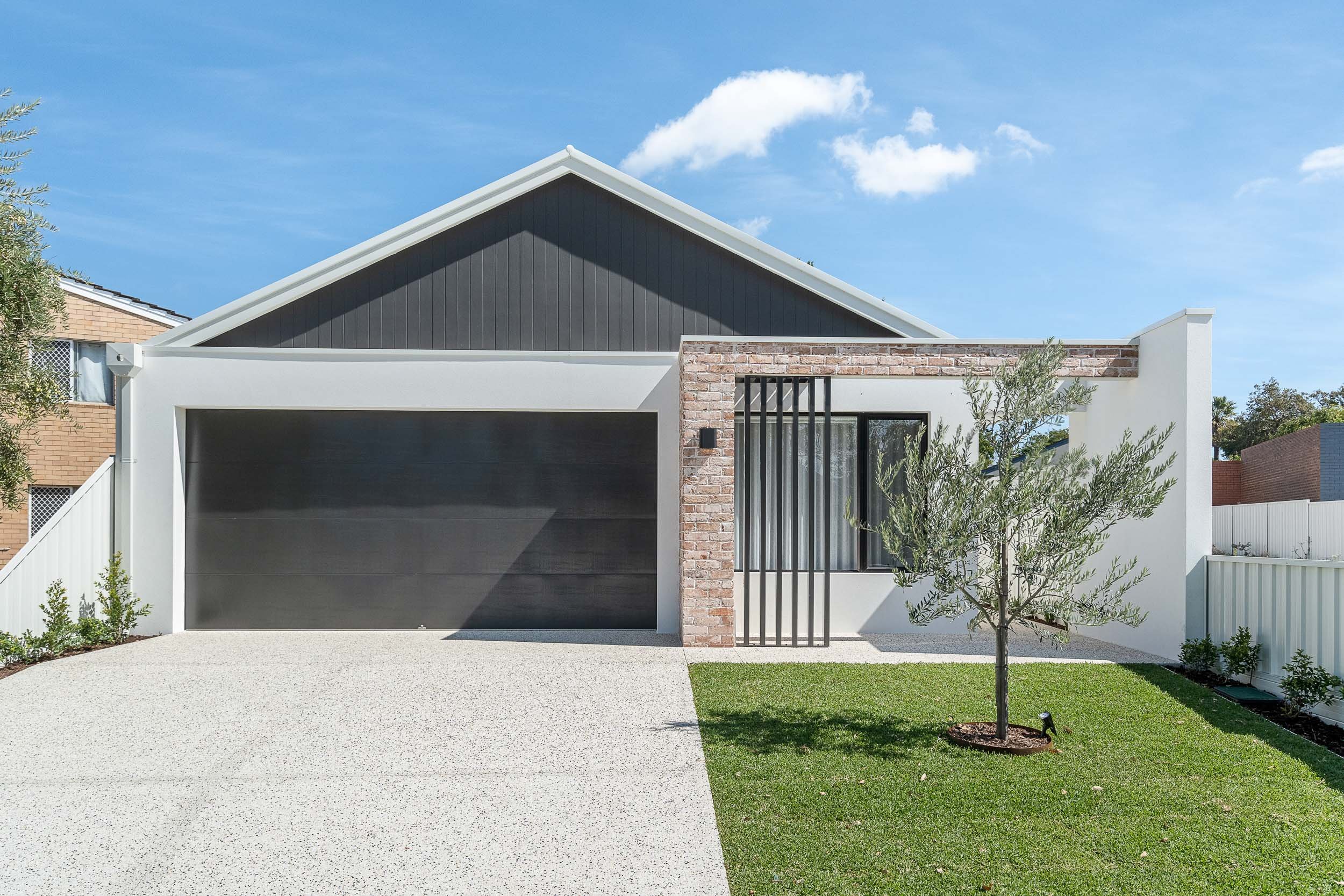 Single-storey home with a gabled roof, dark garage door, paved driveway and landscaped front lawn.