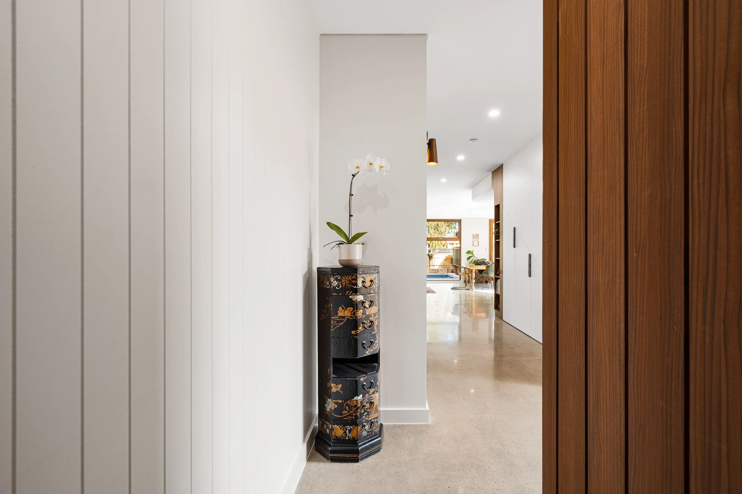Minimal white hallway with a timber door and a decorative vase holding an orchid.