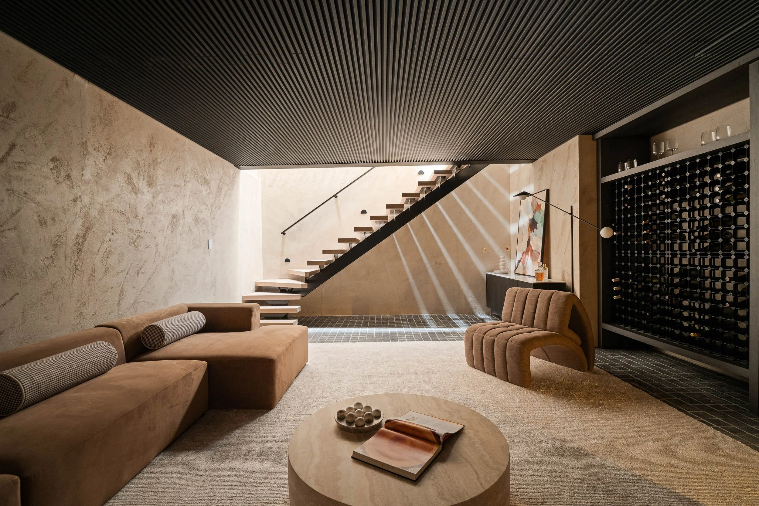 Contemporary lounge with textured walls, a floating staircase, curved sofa and a glass-fronted wine display.