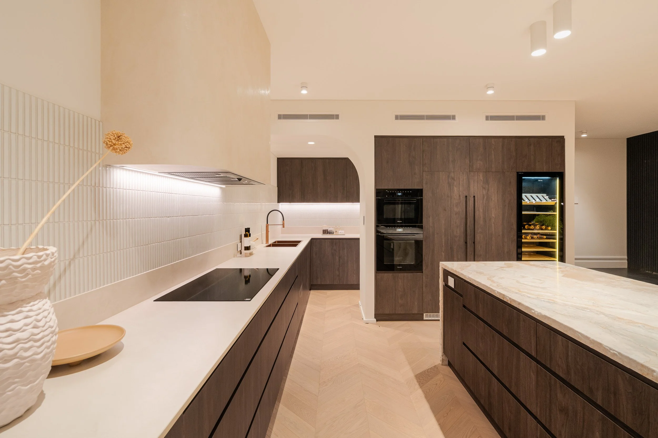 Kitchen with stone benchtops, dark cabinetry and an arched opening to the adjoining space.