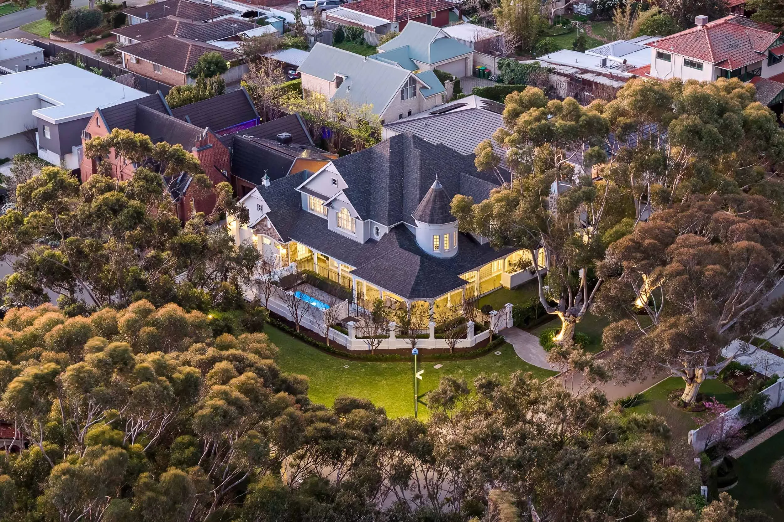 High aerial view of a large home, its roofline and landscaped grounds among mature trees.