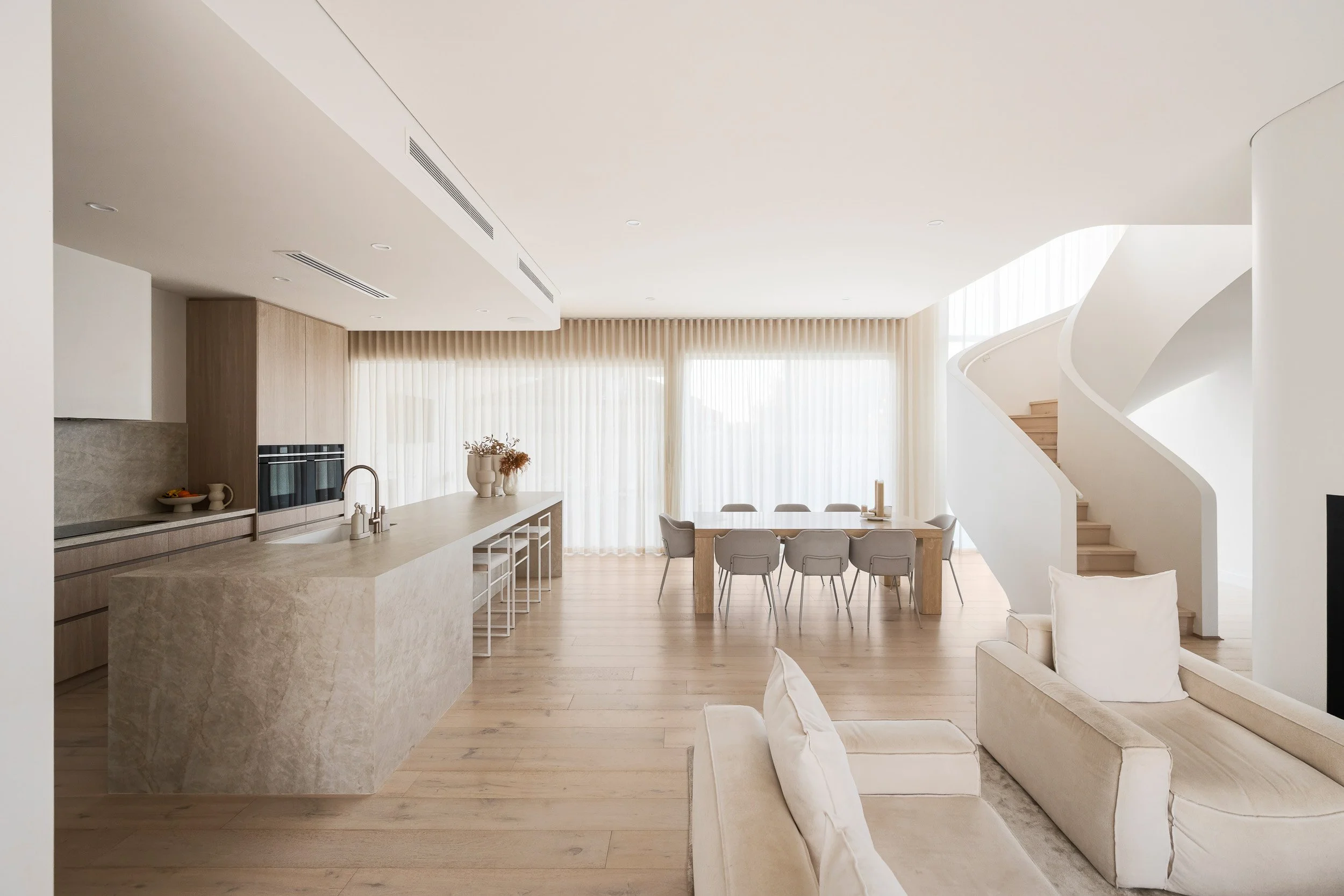 Bright open-plan kitchen and dining area beside a sculptural white staircase.