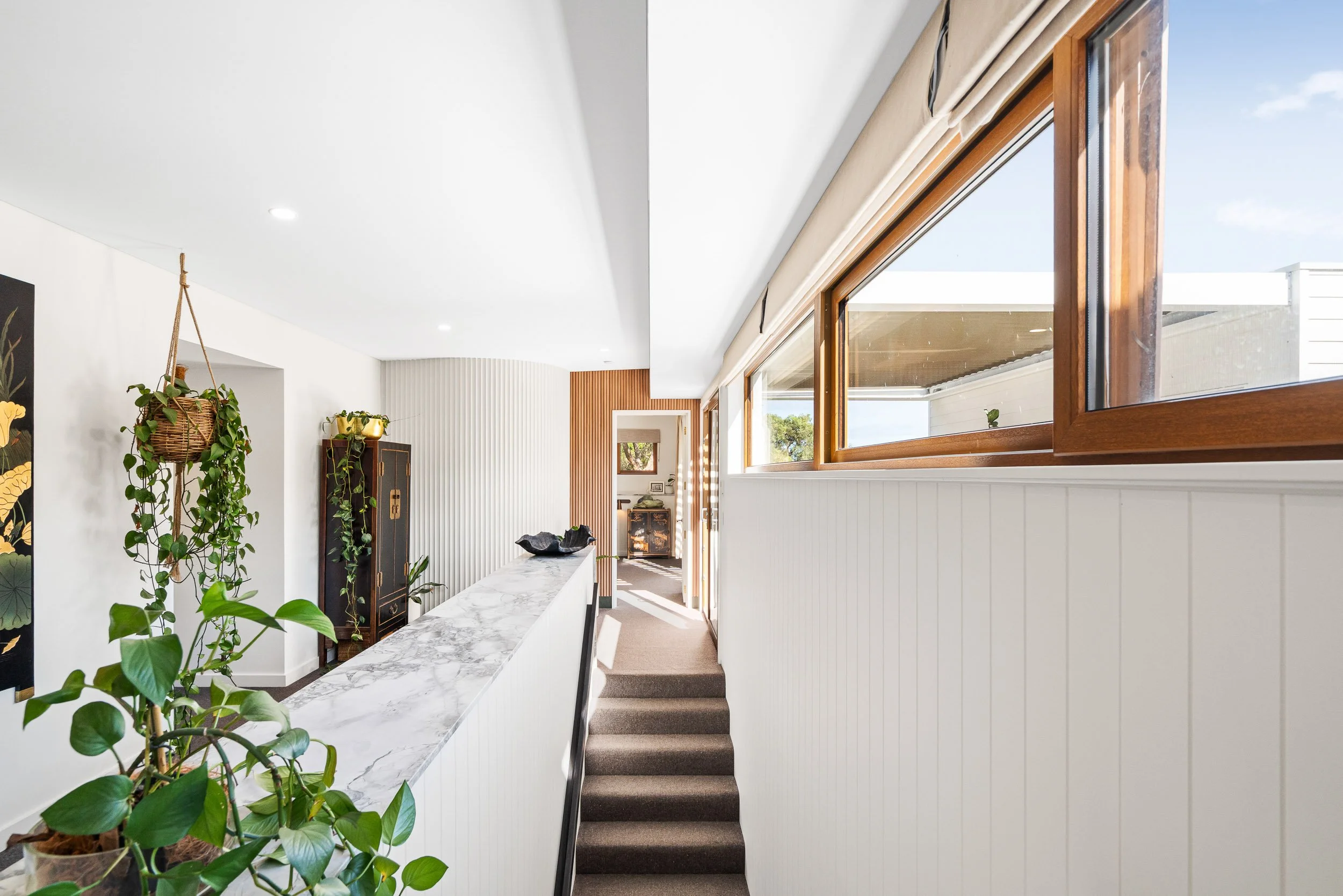 Bright stairwell with indoor planting, white walls and timber-framed windows.