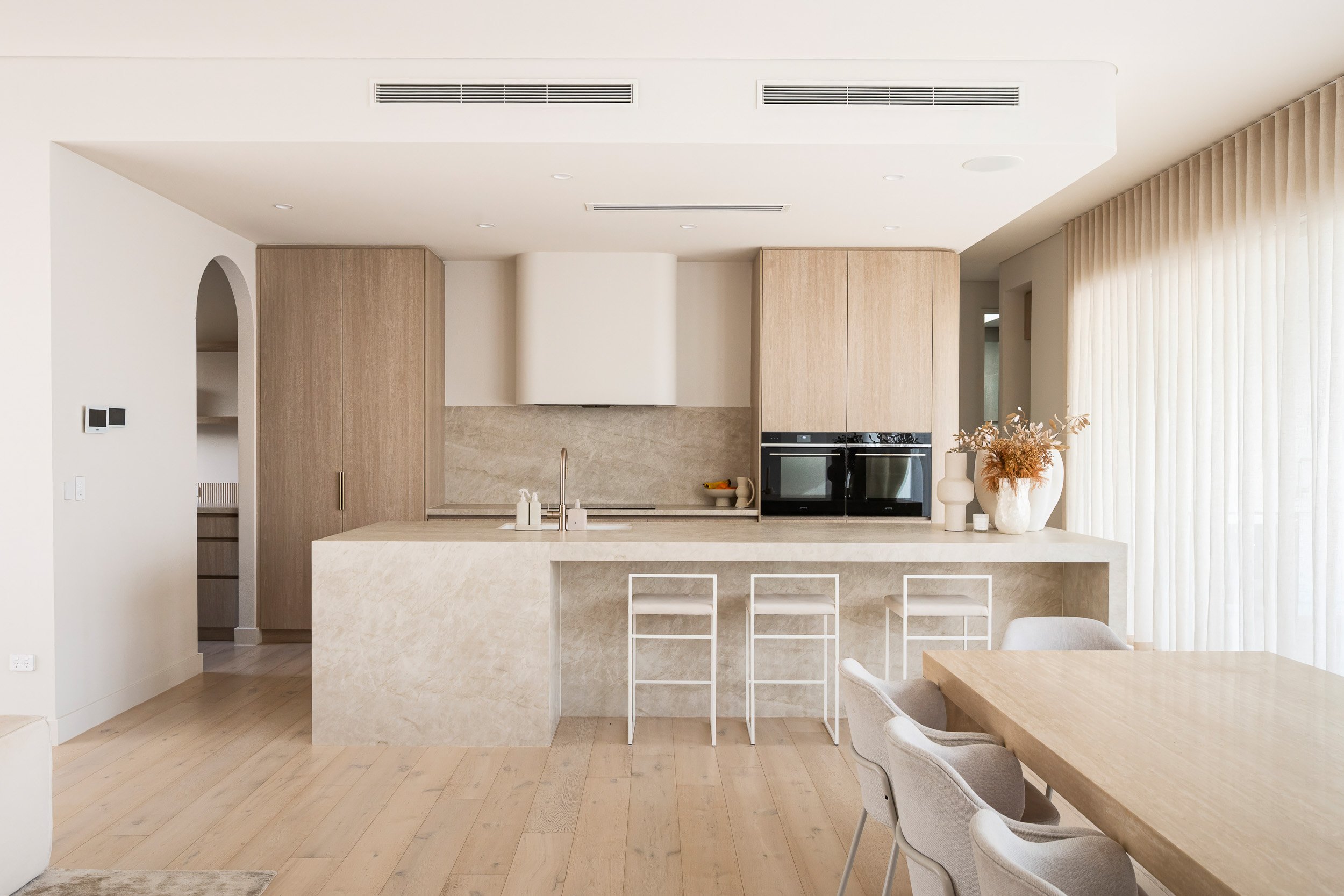Kitchen with pale timber cabinetry, a stone island and white bar stools.