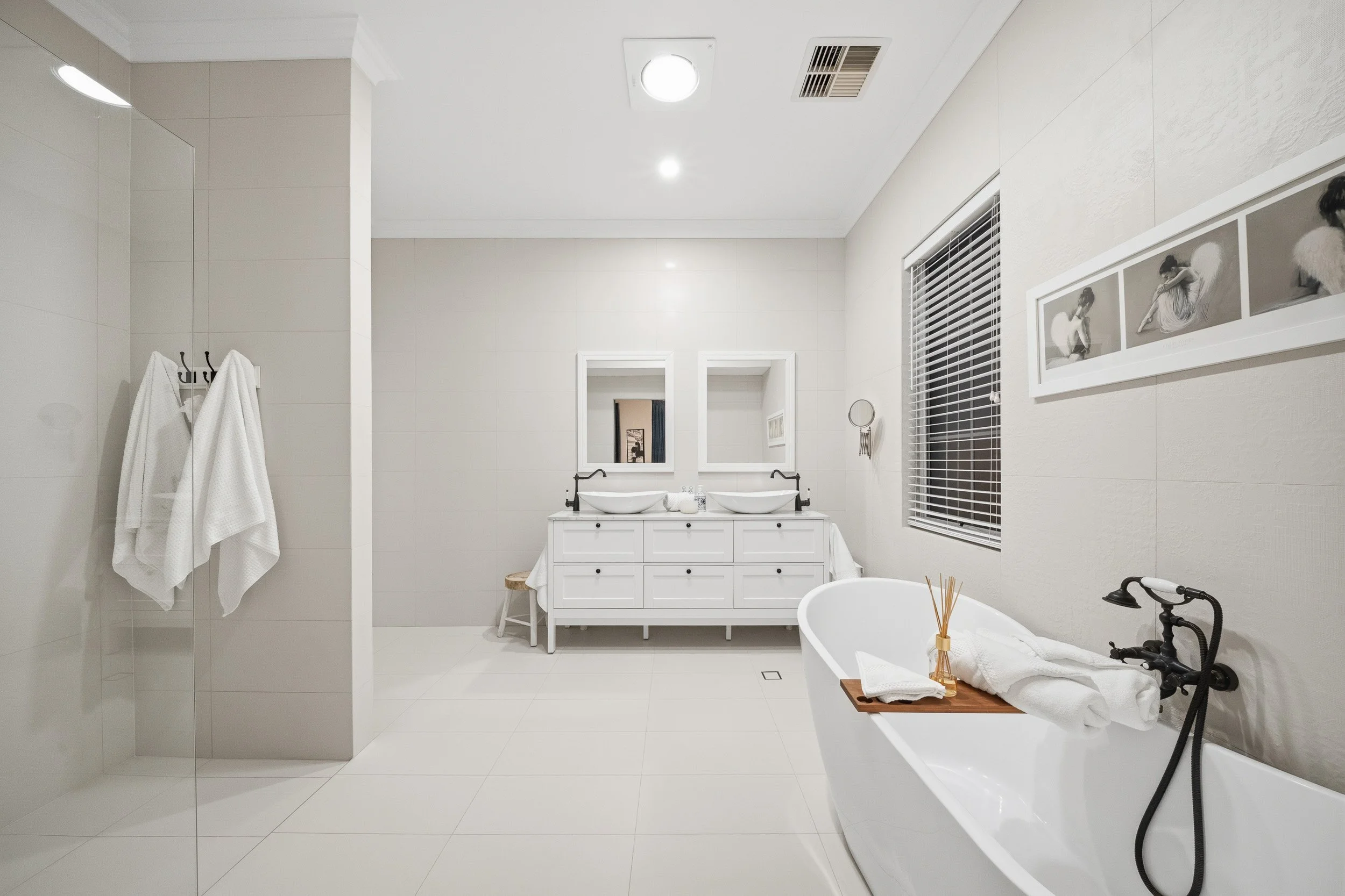 Spacious white bathroom with a freestanding bath, twin-basin vanity and dark tapware.