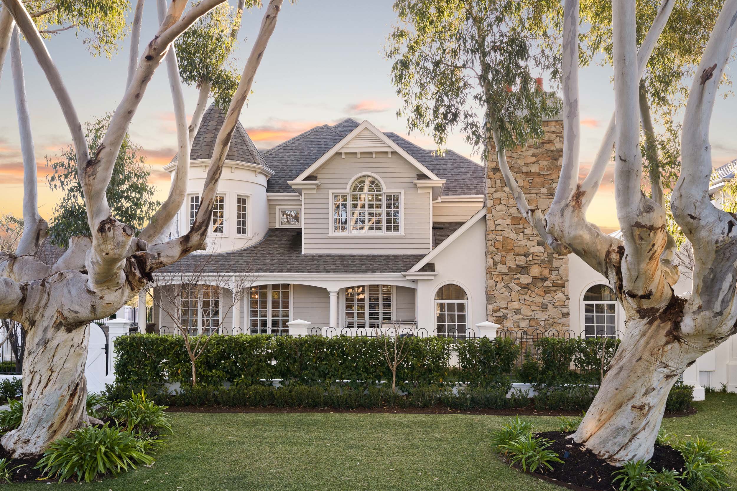 Traditional two-storey home with white weatherboards and decorative gables framed by mature trees.