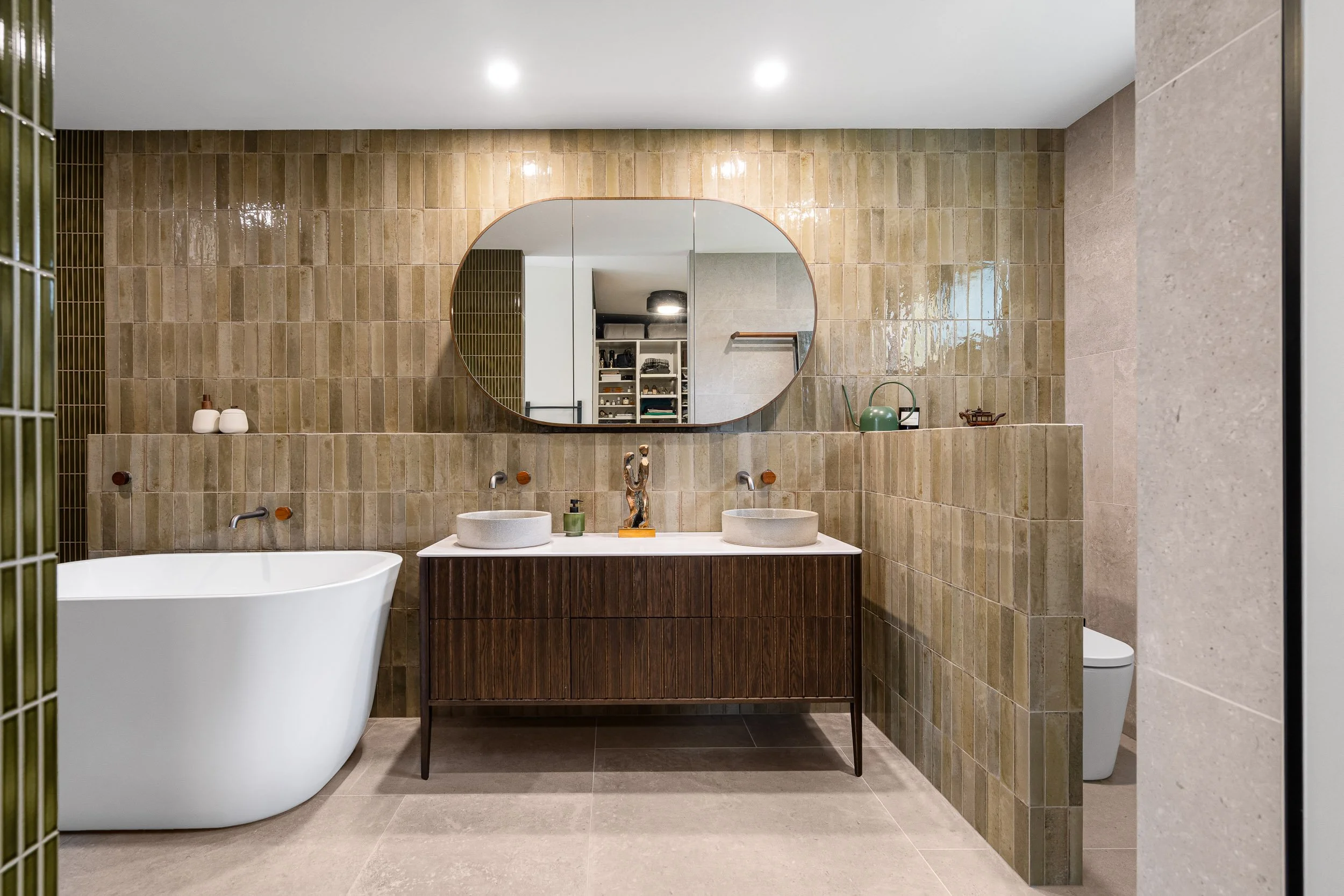 Bathroom with a timber vanity, twin basins, an elongated mirror and textured wall tiles.