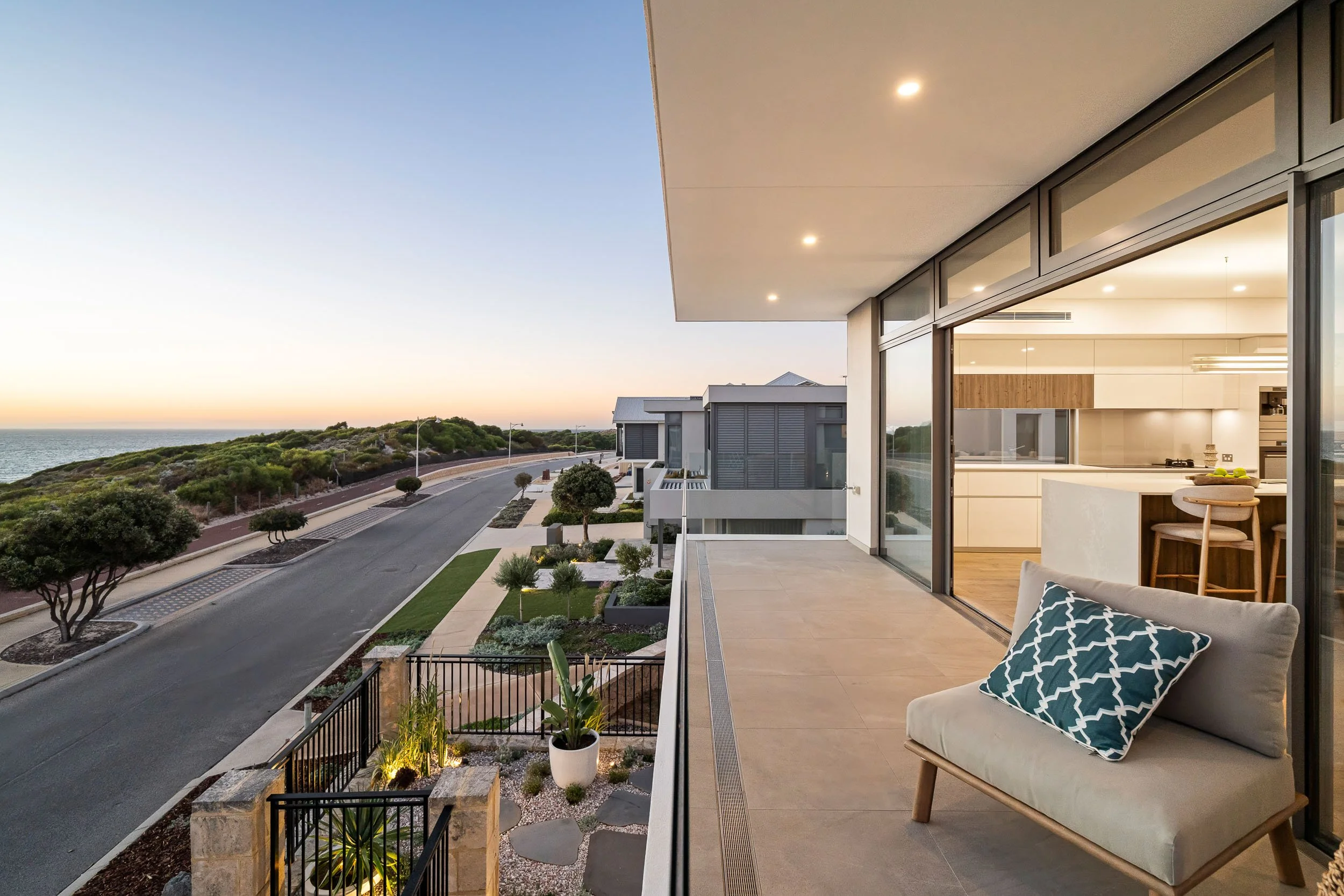 Upper-floor terrace with glass balustrades and coastal views in the evening light.