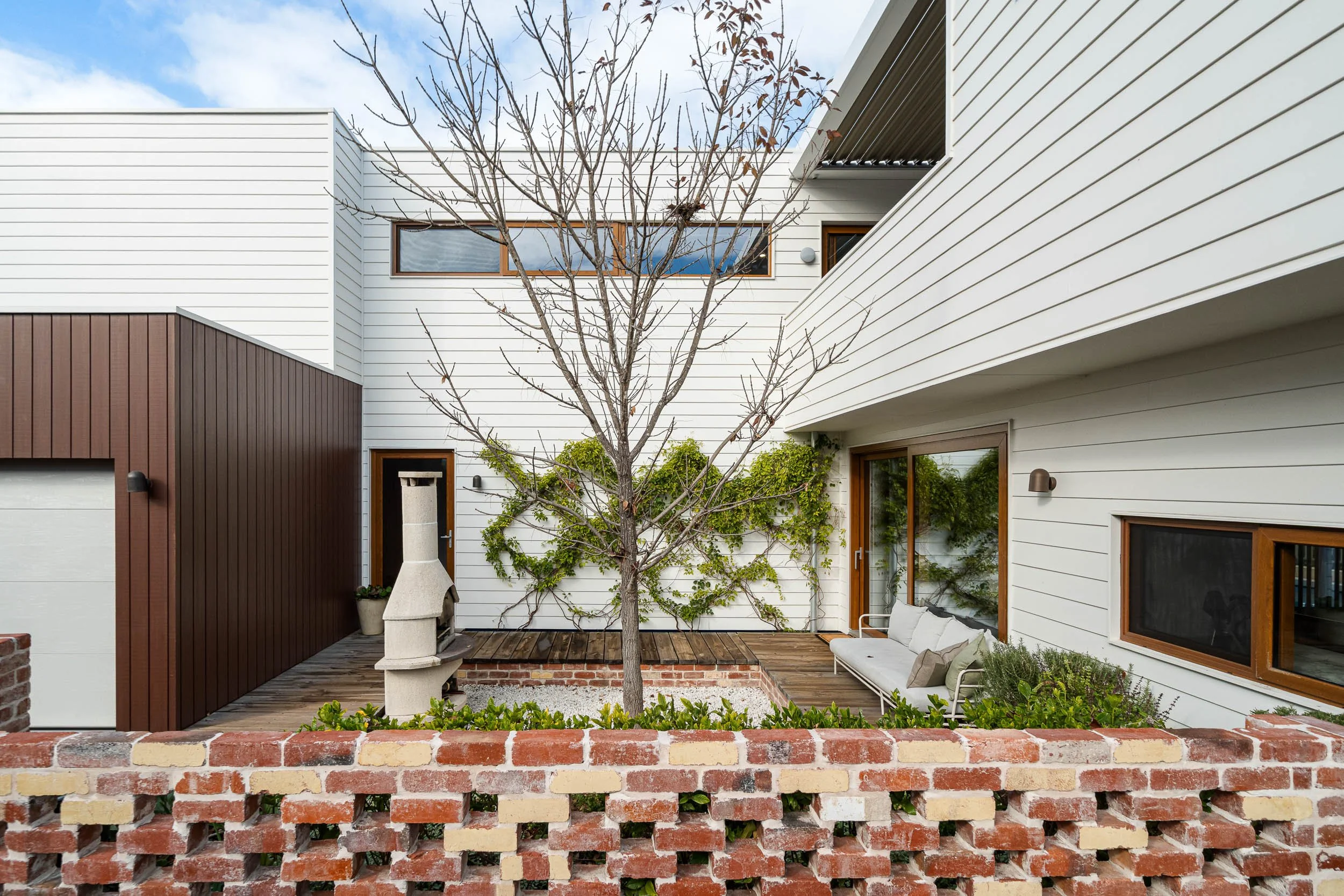 Brick-paved courtyard with a central tree between contemporary residential walls.