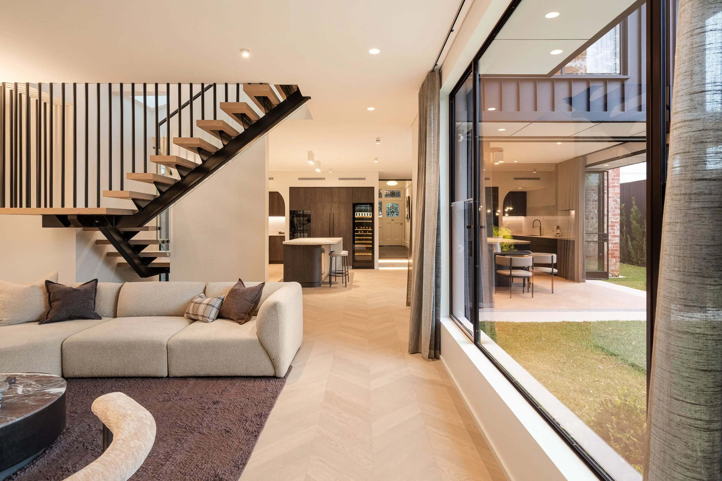 Living room beneath a floating staircase, with a large window overlooking the garden.