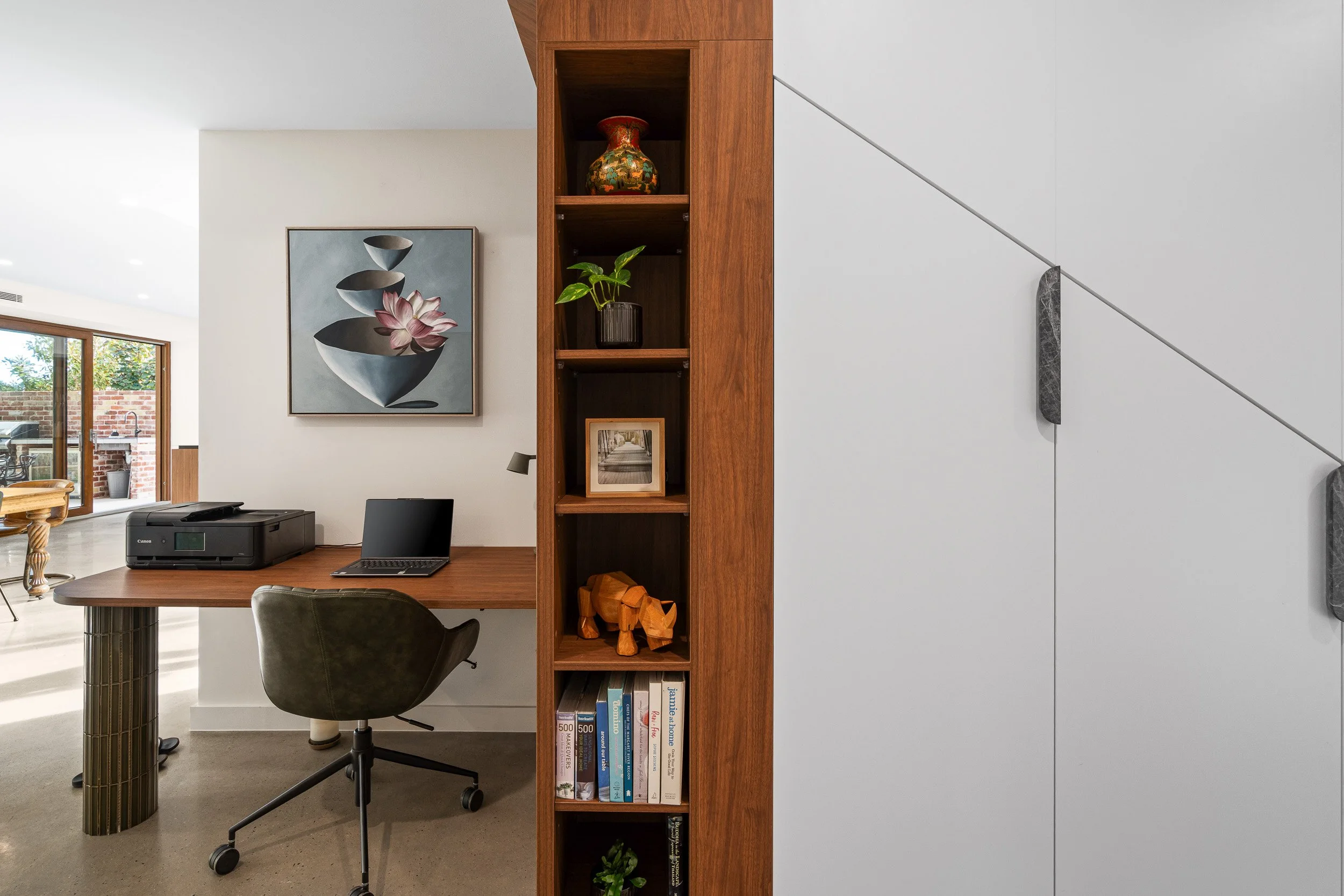 Timber display shelving beside a sitting area with an armchair and framed artwork.