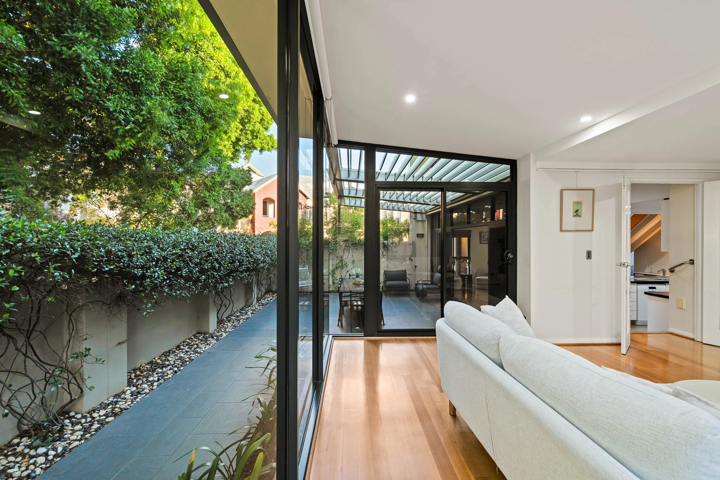 Living area with full-height glazing, timber flooring and a leafy side garden.