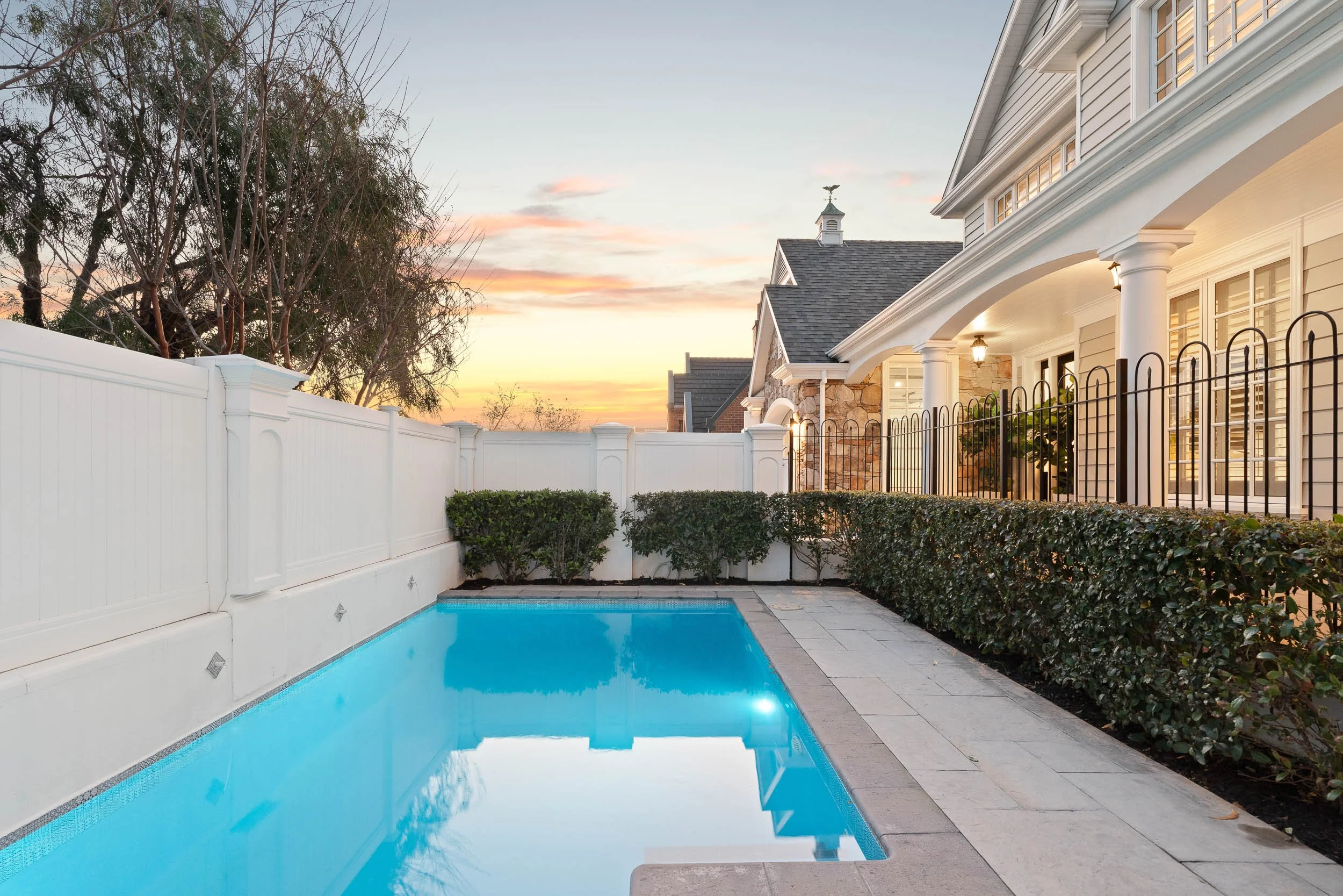 Swimming pool beside an illuminated traditional home at twilight.