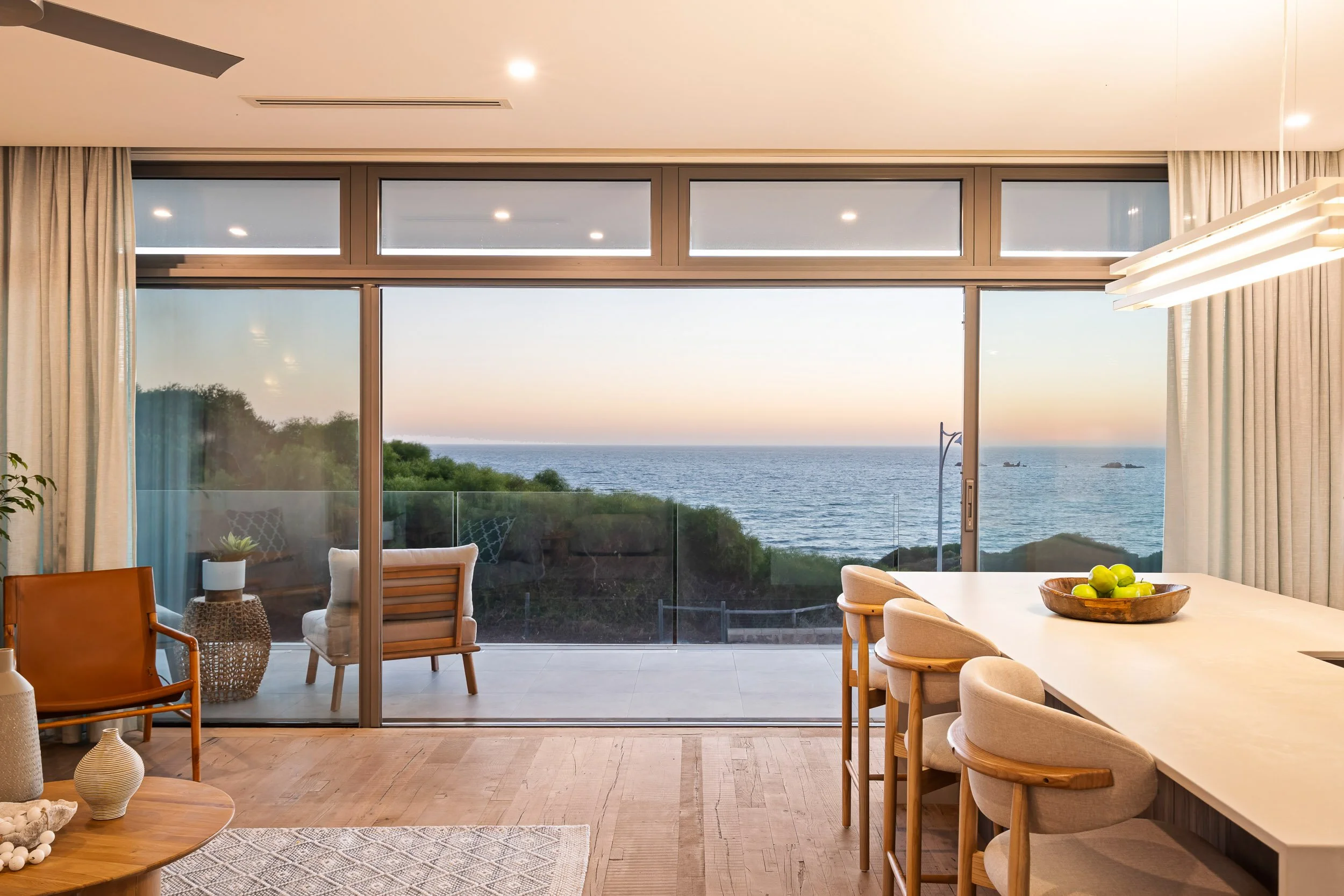 Dining area with wide glass doors framing a coastal terrace and ocean view.