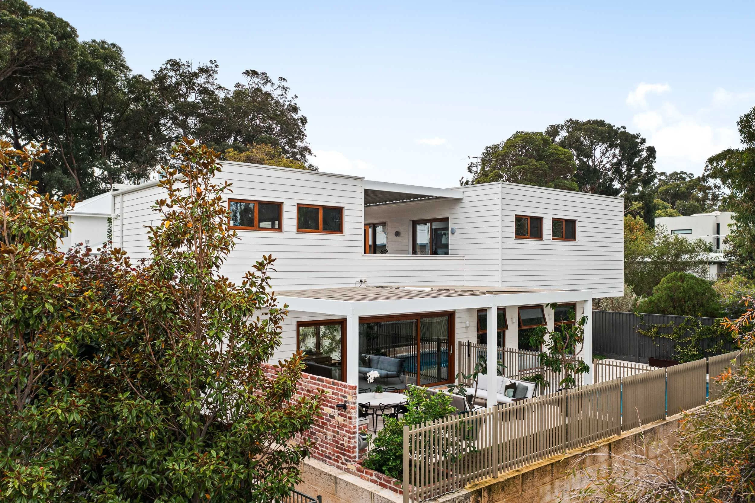 White-clad contemporary home with a balcony framed by mature trees and garden planting.