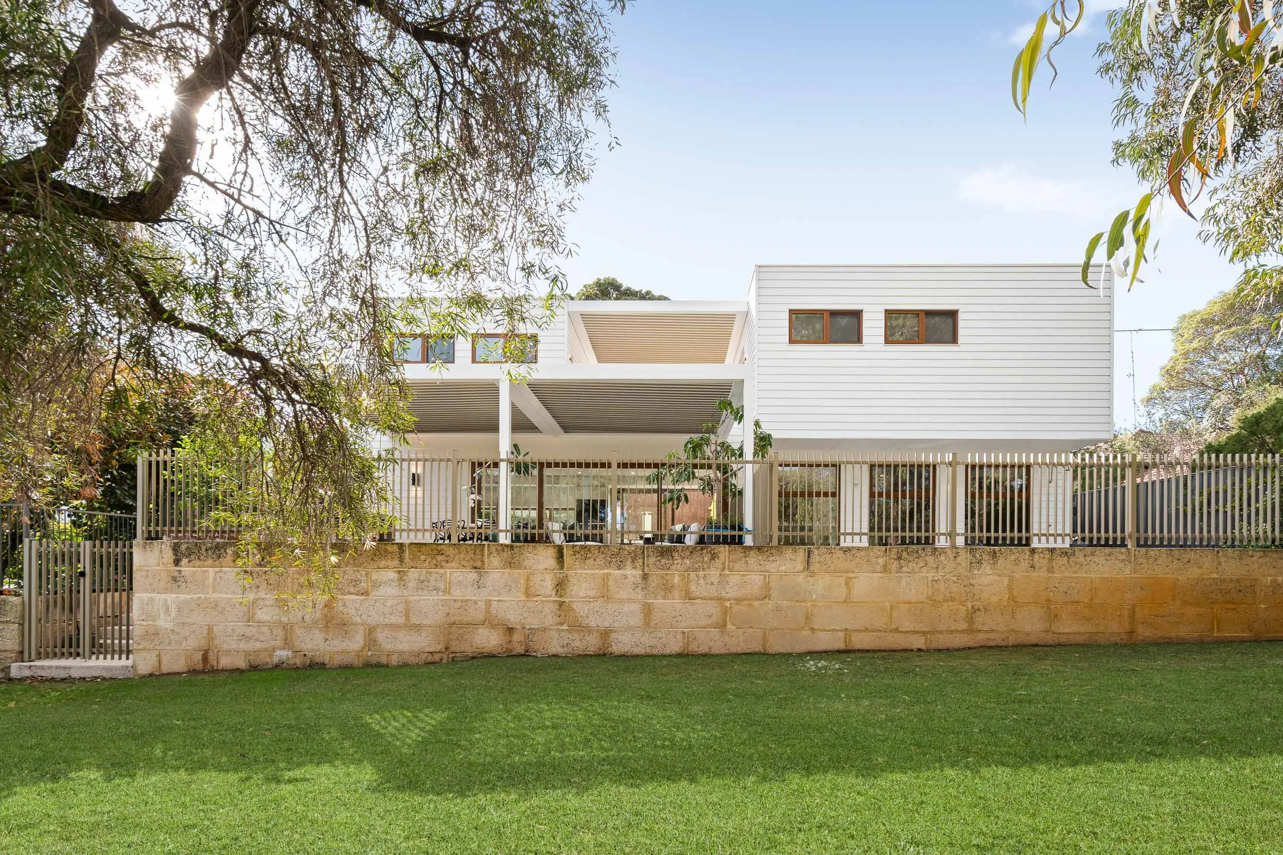 Contemporary white-clad home with a raised terrace, stone garden wall and established trees.