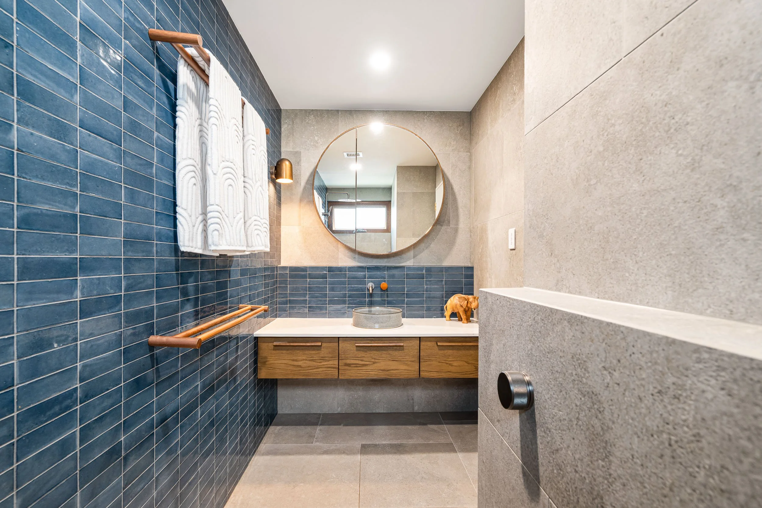 Bathroom with patterned blue tiles, a circular mirror and timber vanity.