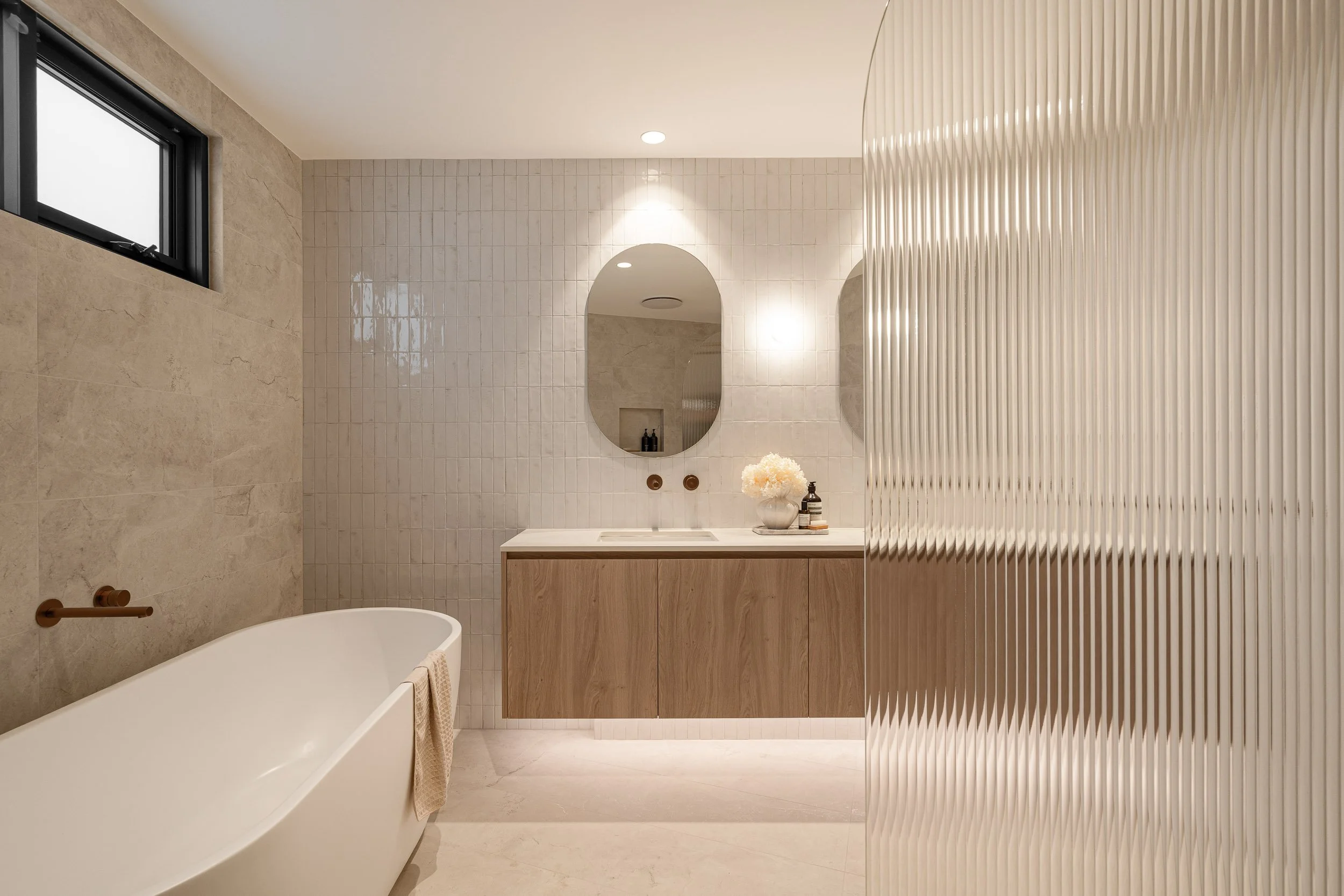 Bathroom with an oval mirror, timber vanity and frameless glass shower screen.