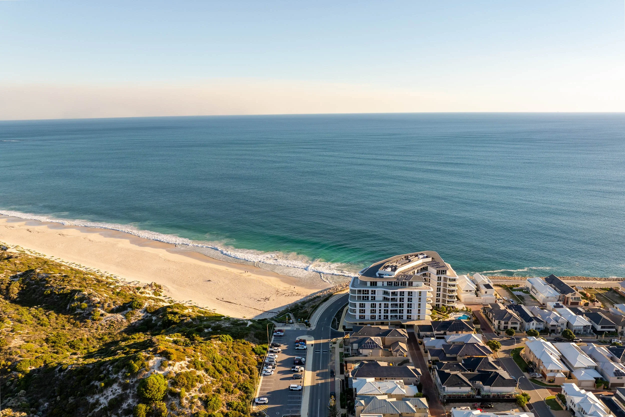 Coastal aerial showing beachfront development, sandy shoreline and open ocean.