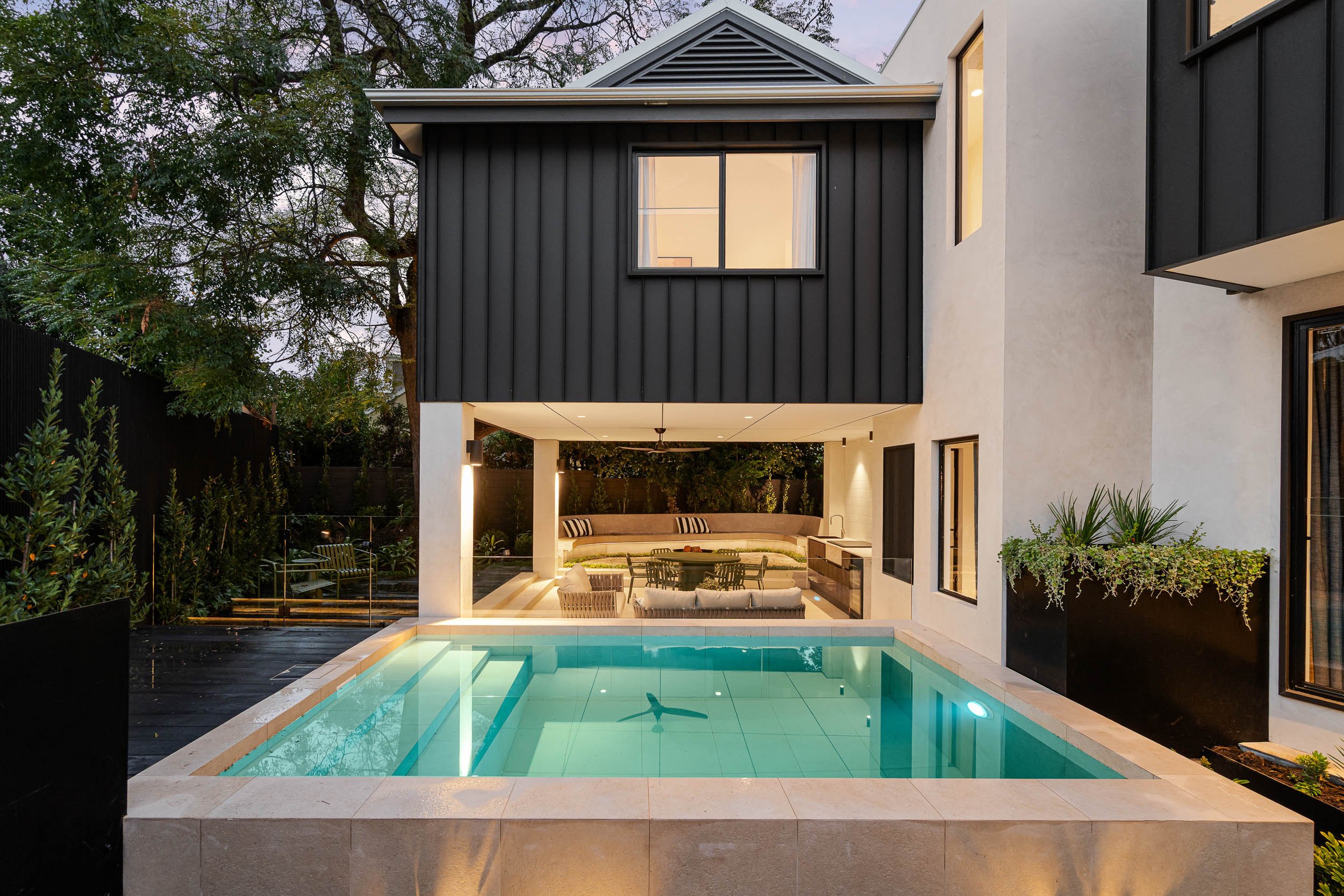 Dark-clad contemporary home overlooking an illuminated swimming pool at twilight.