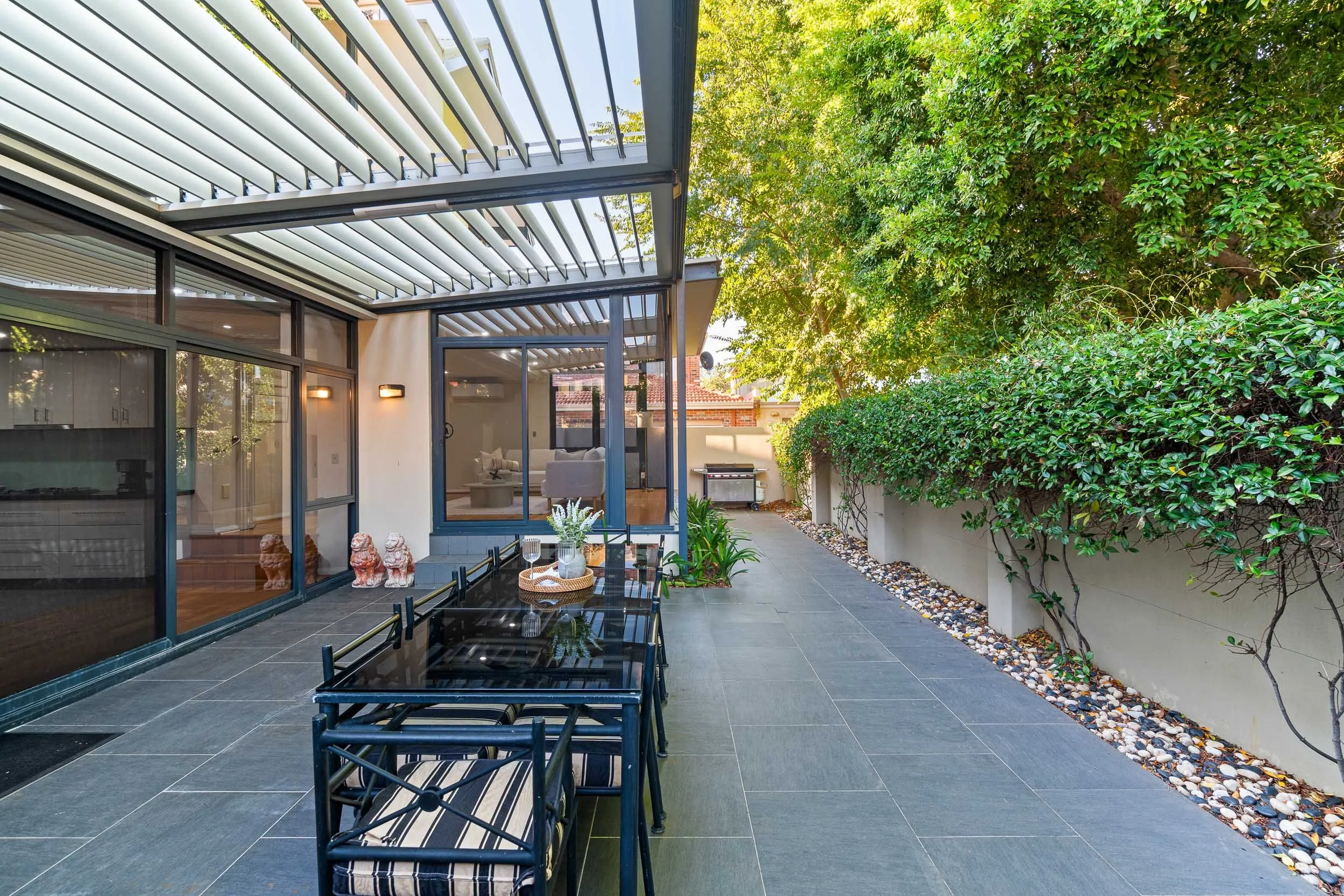 Courtyard dining area beneath a slatted pergola beside climbing greenery.