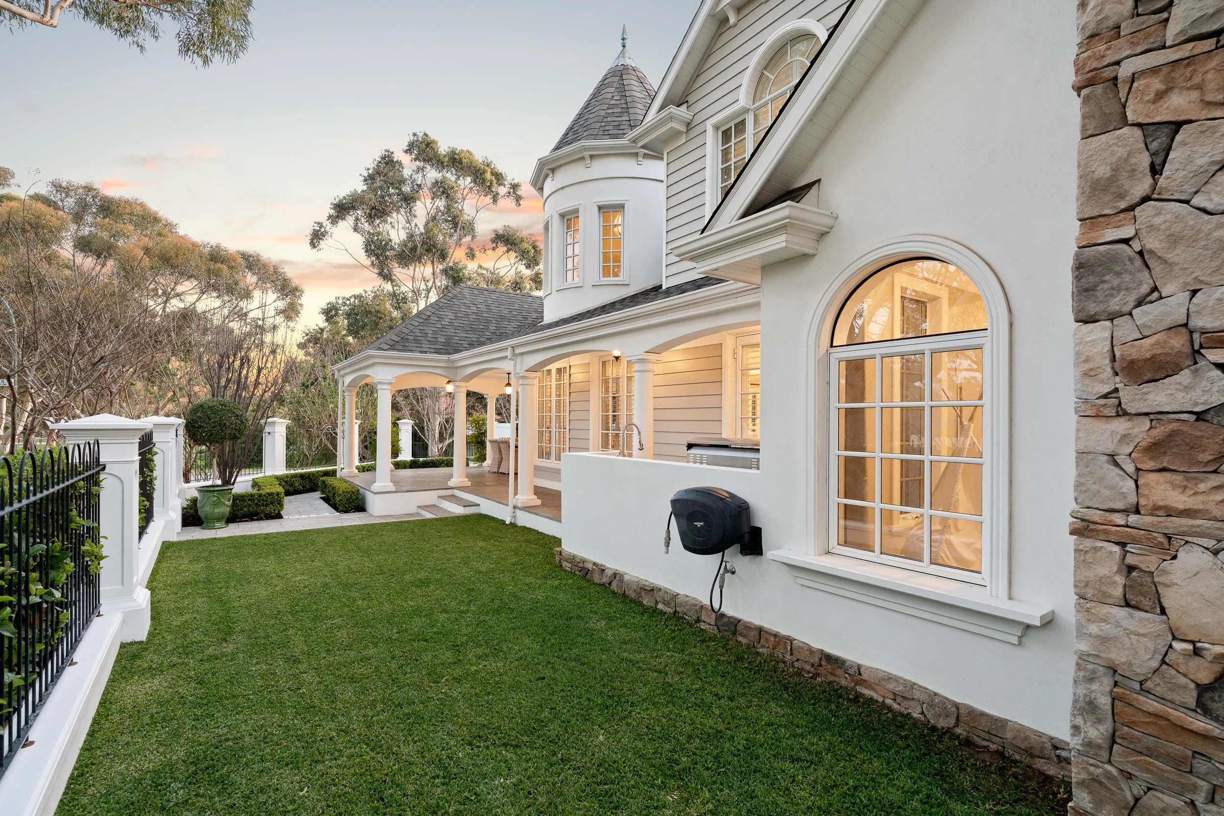 Traditional home at twilight with a turret, illuminated arched windows and a neatly edged lawn.