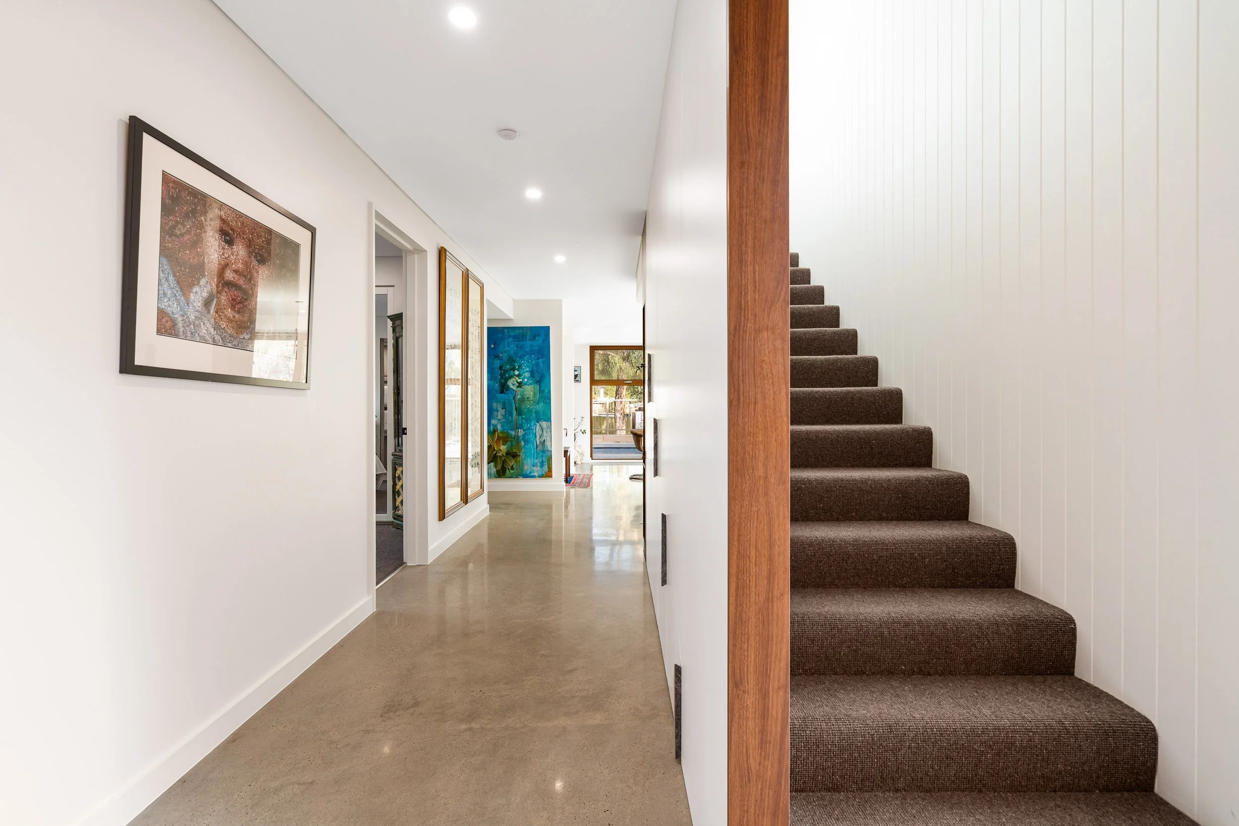 Interior hallway with polished flooring and a carpeted staircase beside timber detailing.