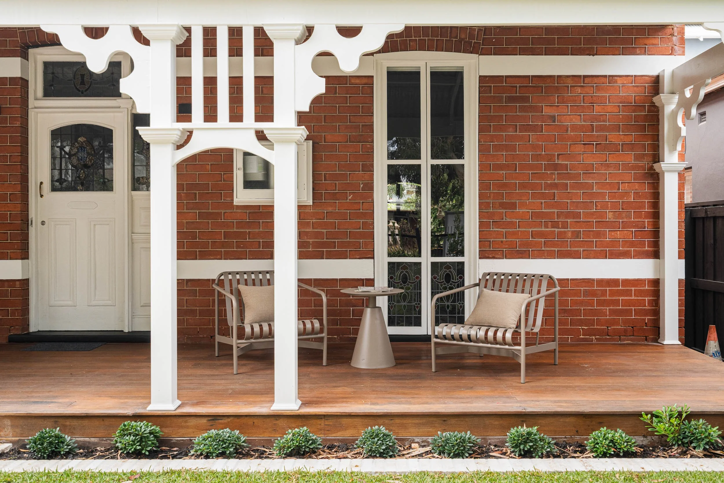 Traditional red-brick veranda with decorative white timber fretwork, outdoor armchairs and a timber deck.