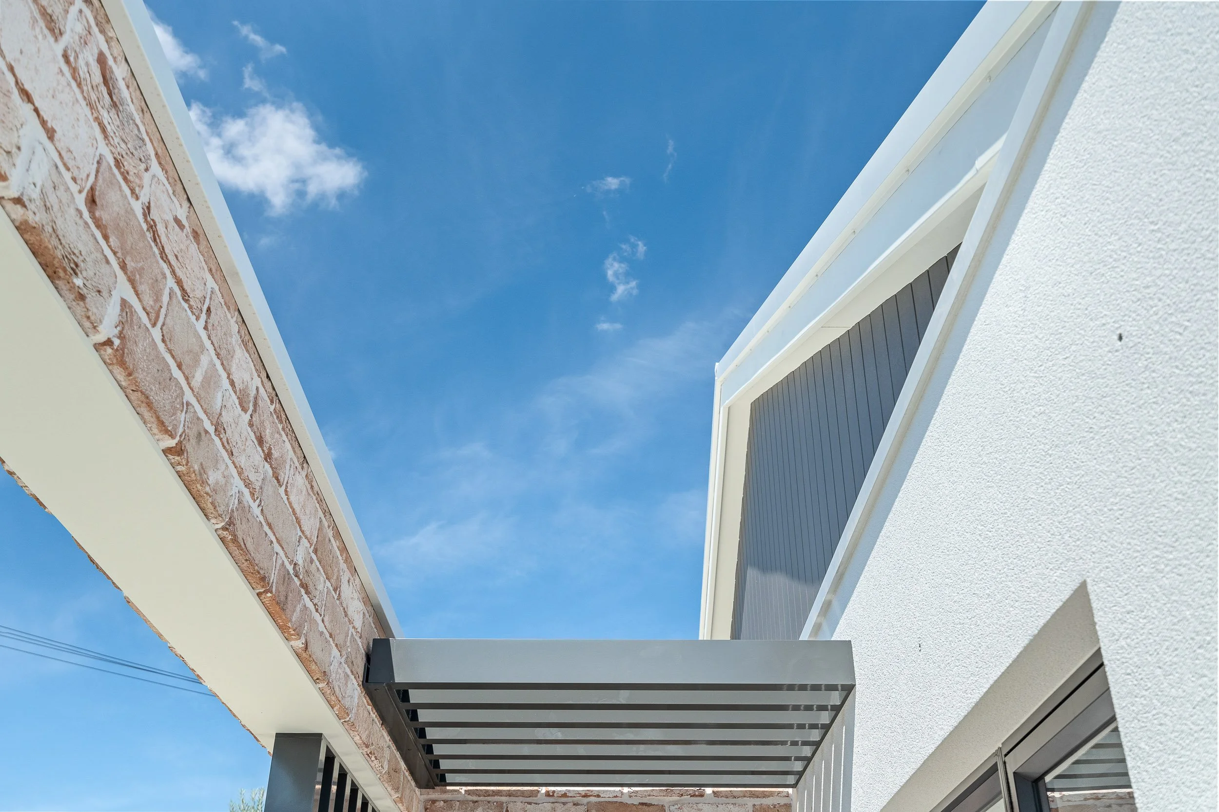 Upward view of a contemporary white-brick facade and balcony against a blue sky.