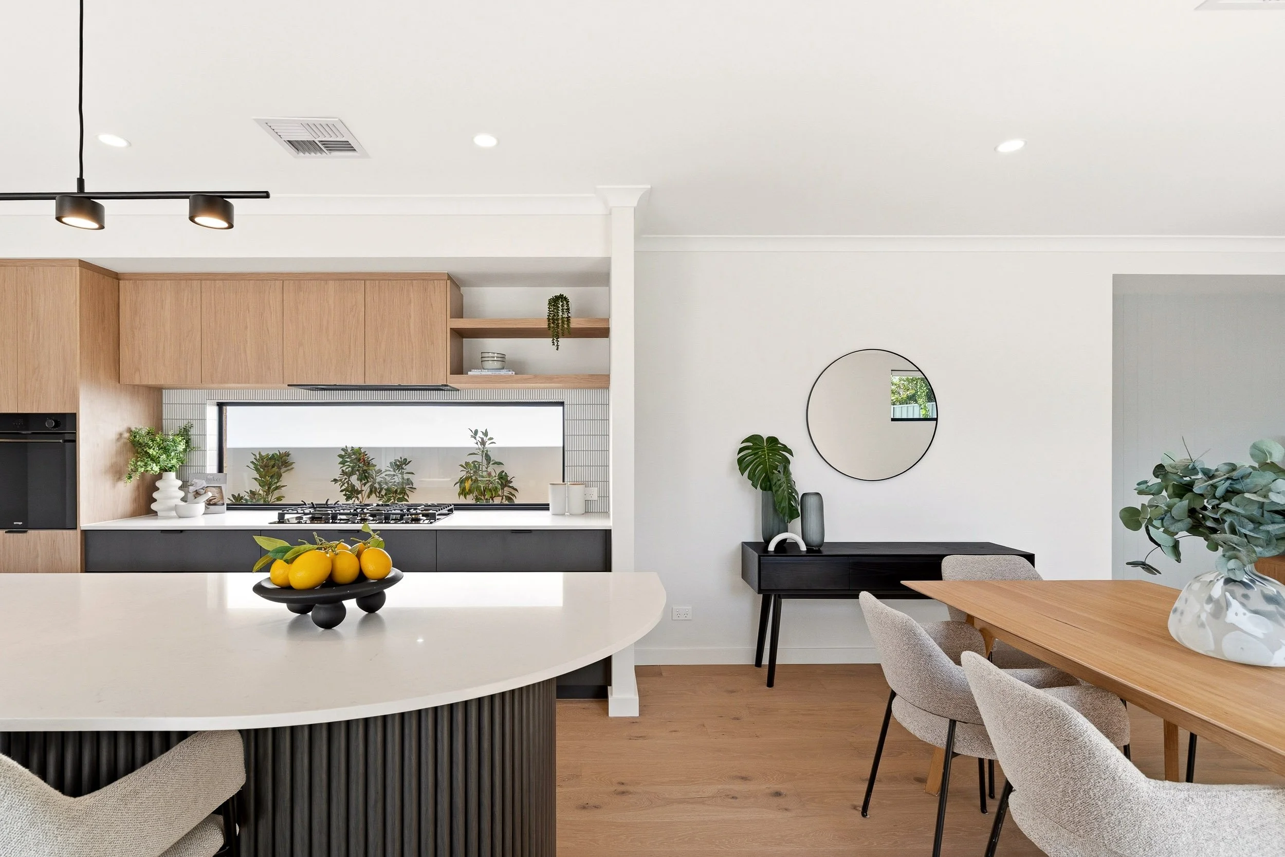 Open-plan kitchen and dining area with a white island benchtop, timber cabinetry and pale flooring.