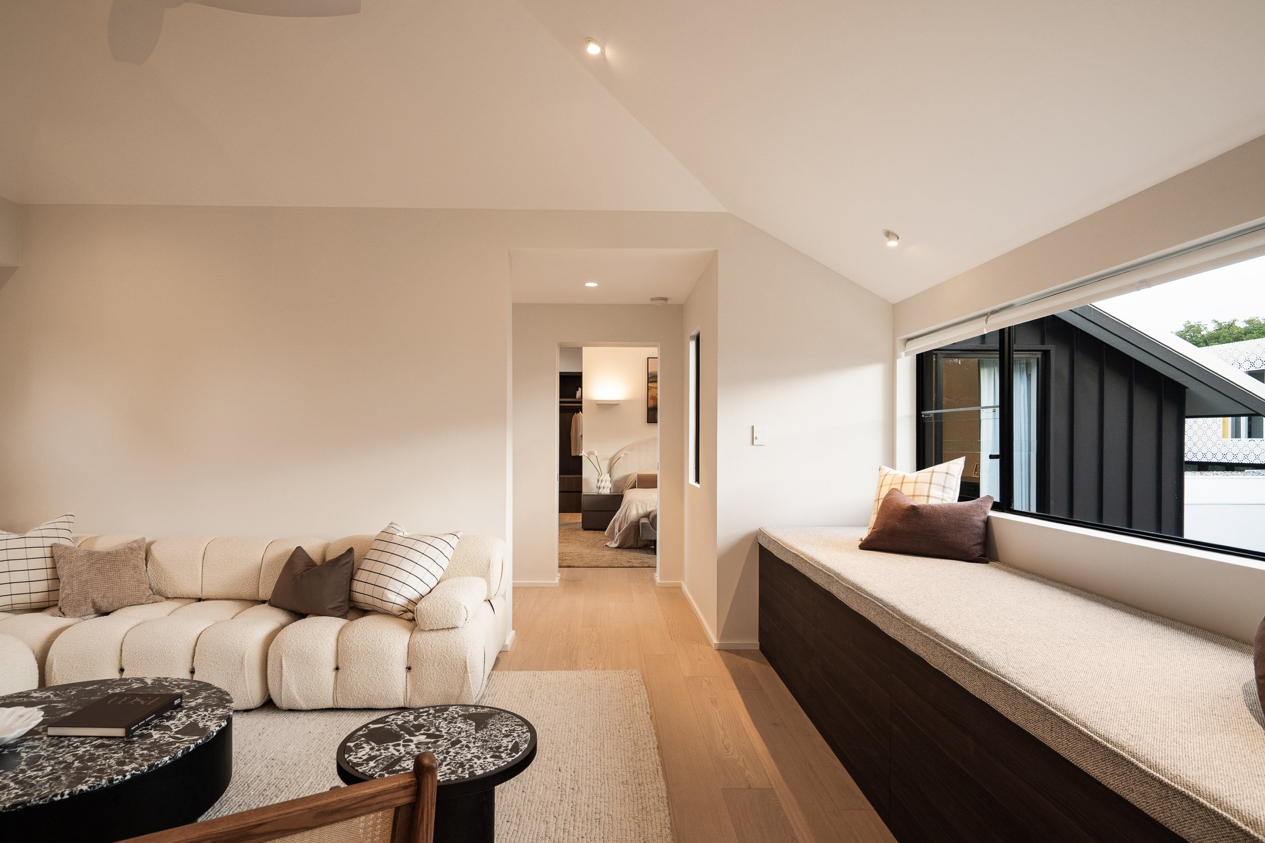 Living room with a curved cream sofa, dark stone coffee tables and a built-in window seat.