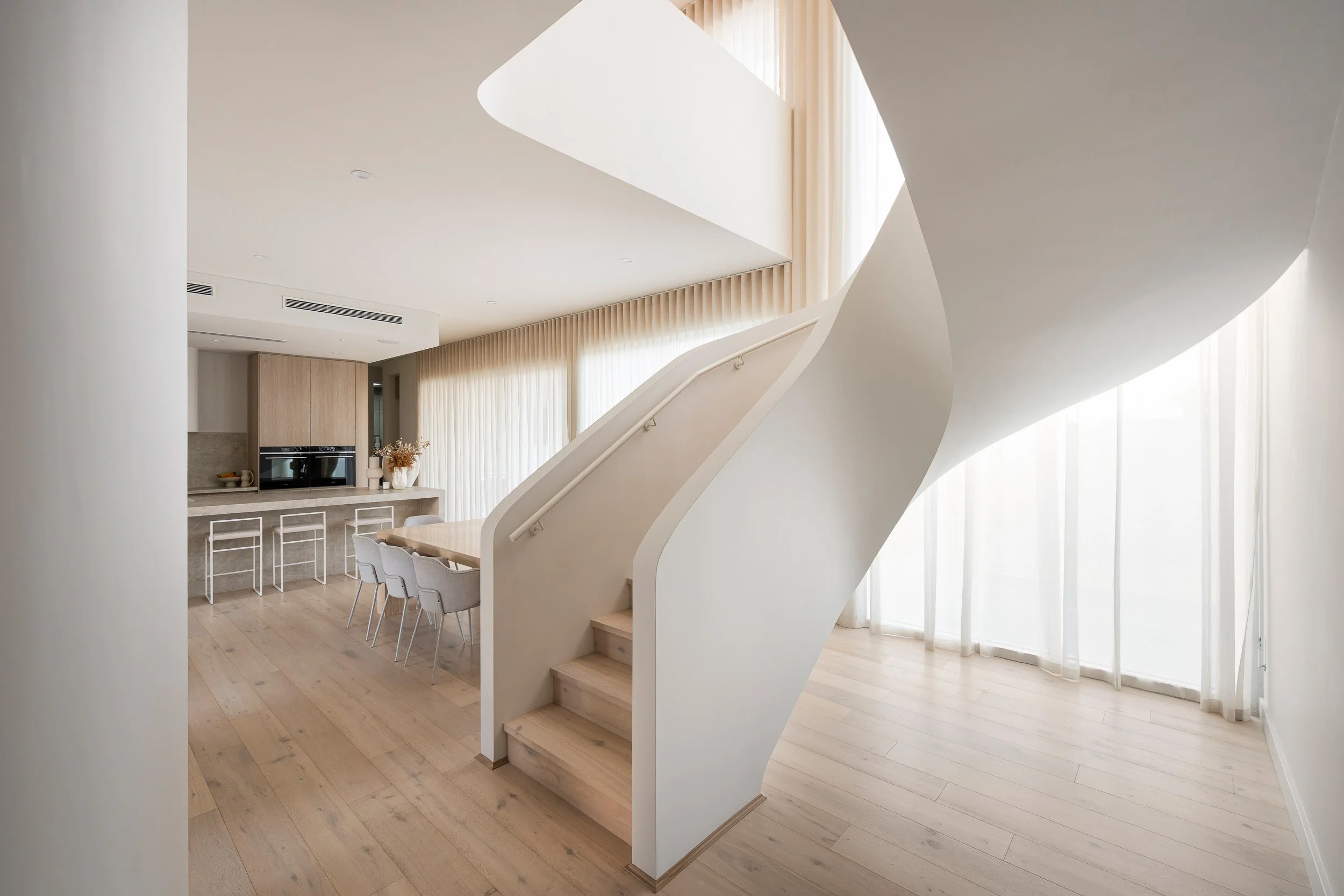 Sculptural white staircase curving through a bright open-plan interior.