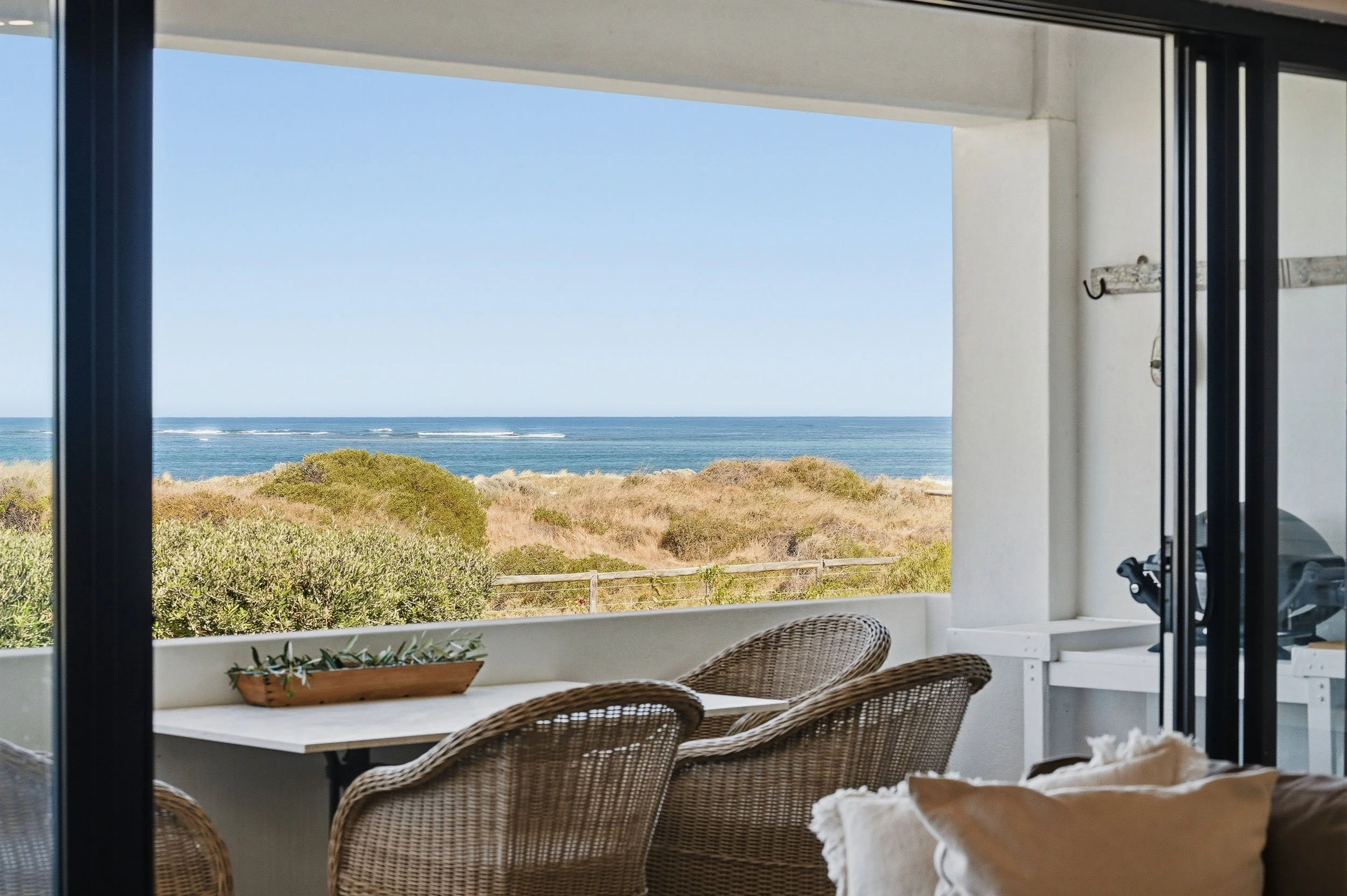 Balcony with woven outdoor seating and views across coastal dunes to the ocean.
