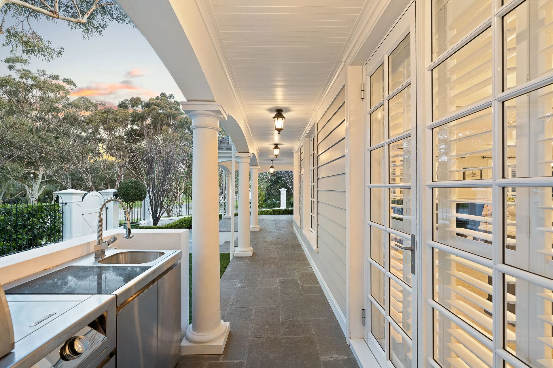 Long covered veranda with white timber posts, decorative windows and hanging lanterns.