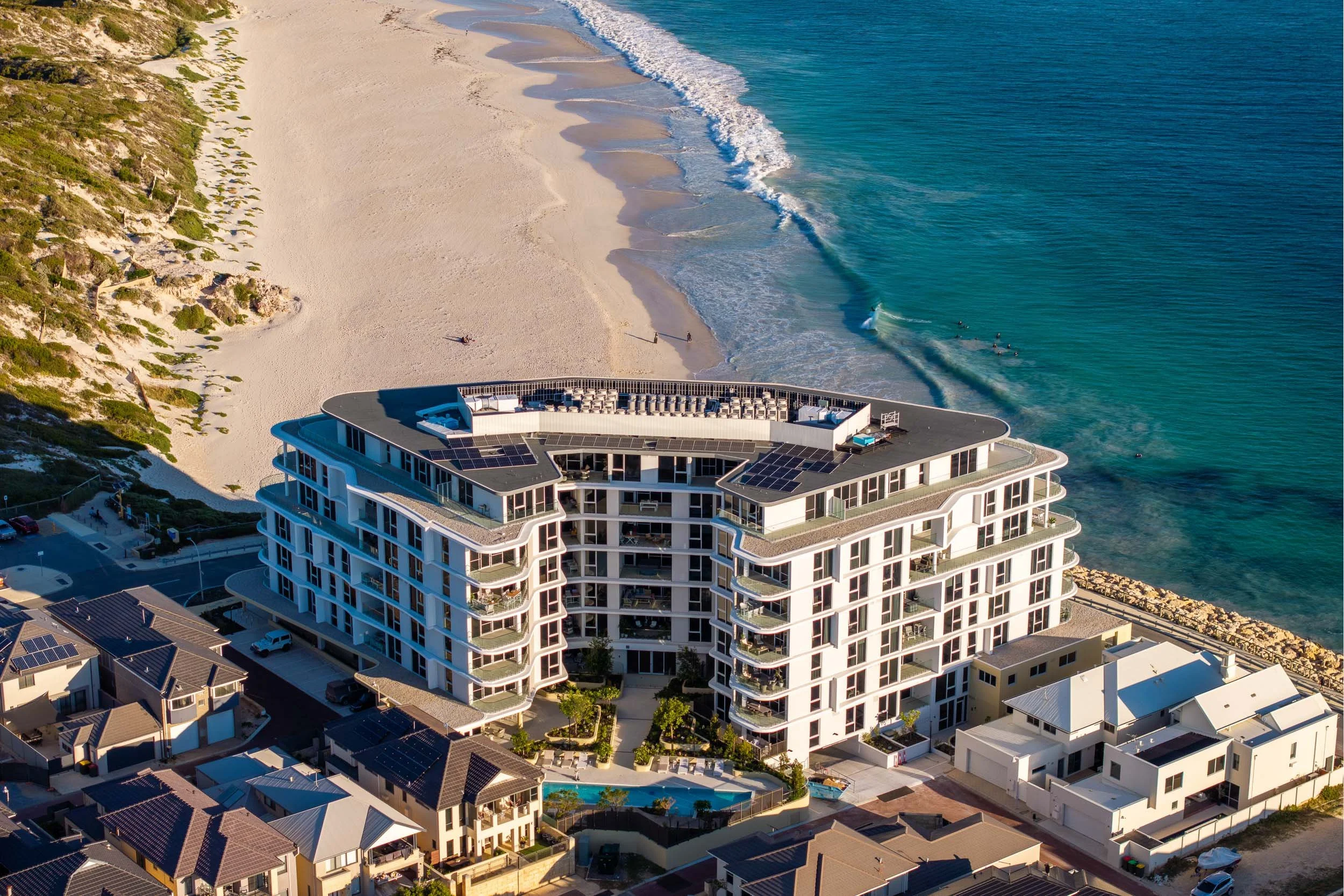 Aerial view of a beachfront apartment building beside a sandy shoreline.