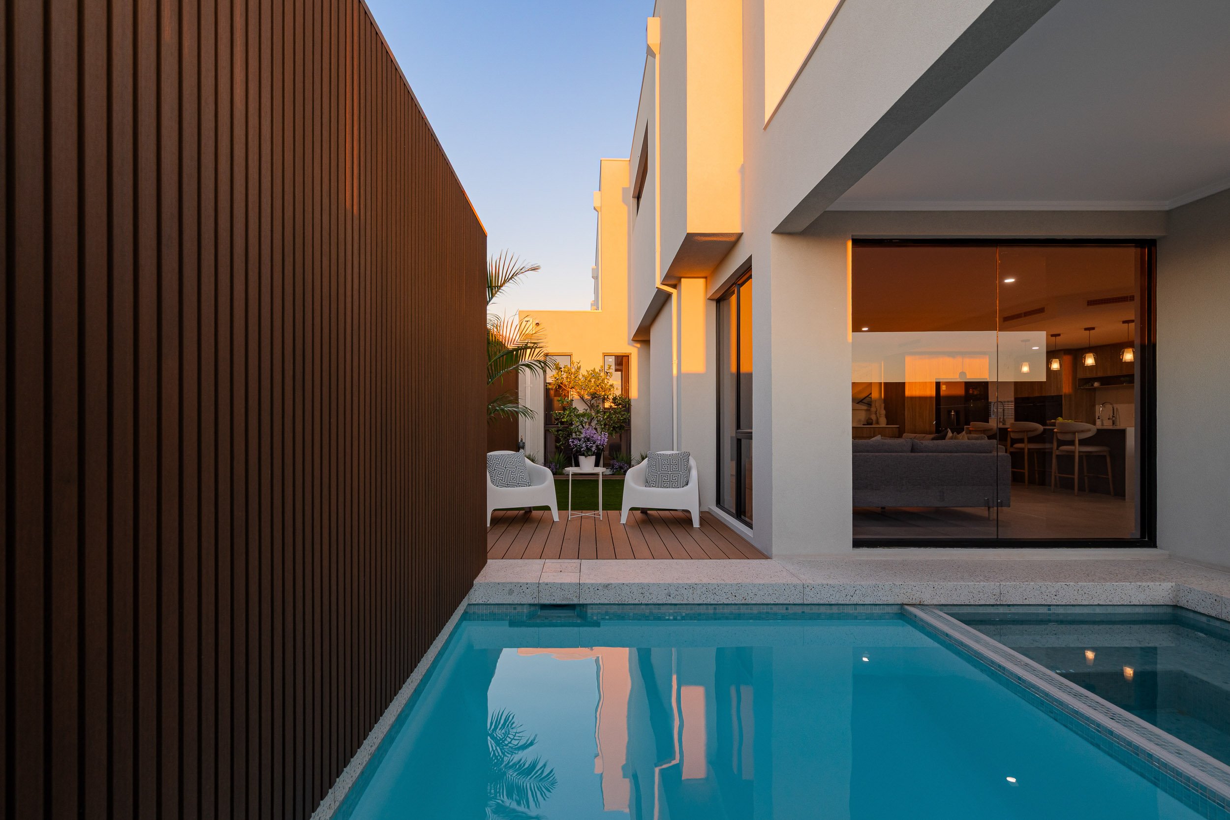 Narrow swimming pool courtyard between a timber screen and a contemporary home at twilight.