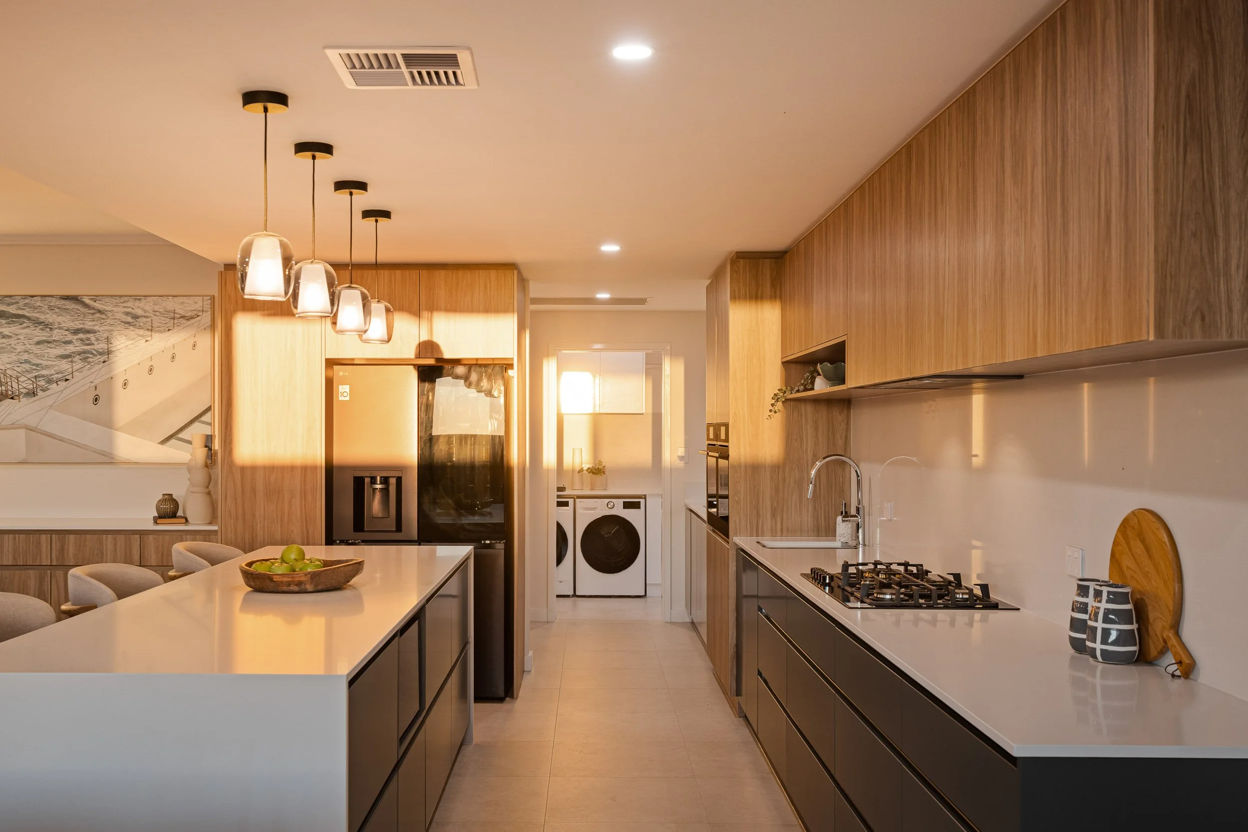 Contemporary galley kitchen with timber overhead cabinets, dark drawers, a stone island and glass pendant lights.