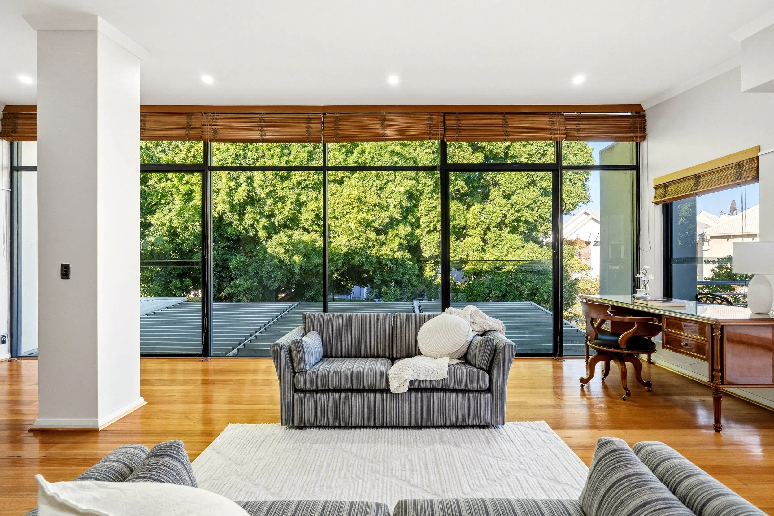 Living room with striped sofas, timber floors and full-height windows overlooking a leafy garden.