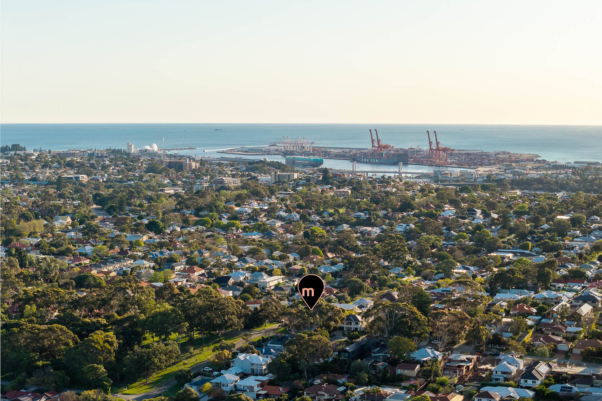 Wide aerial view across a coastal neighbourhood towards the ocean.
