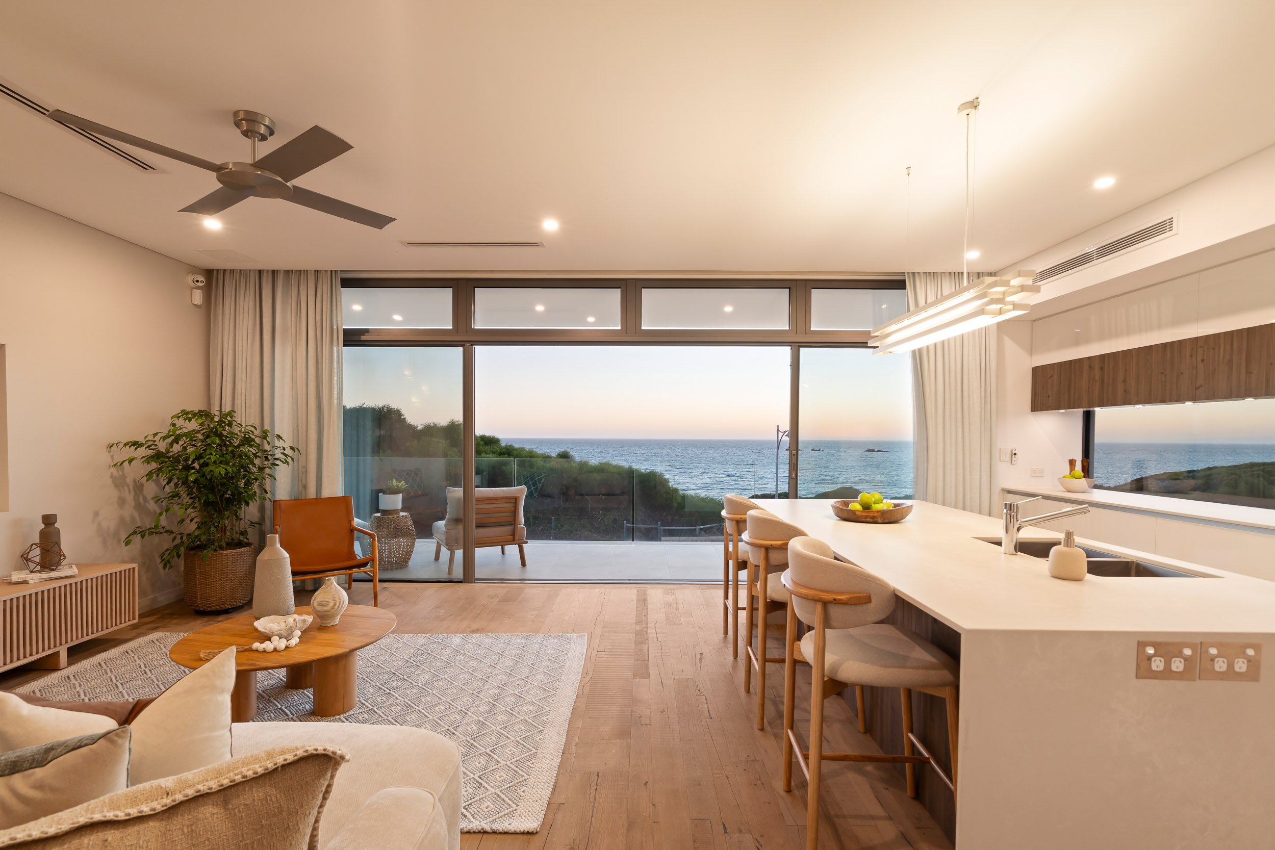 Open-plan kitchen and living room opening to an ocean-facing terrace in the evening.